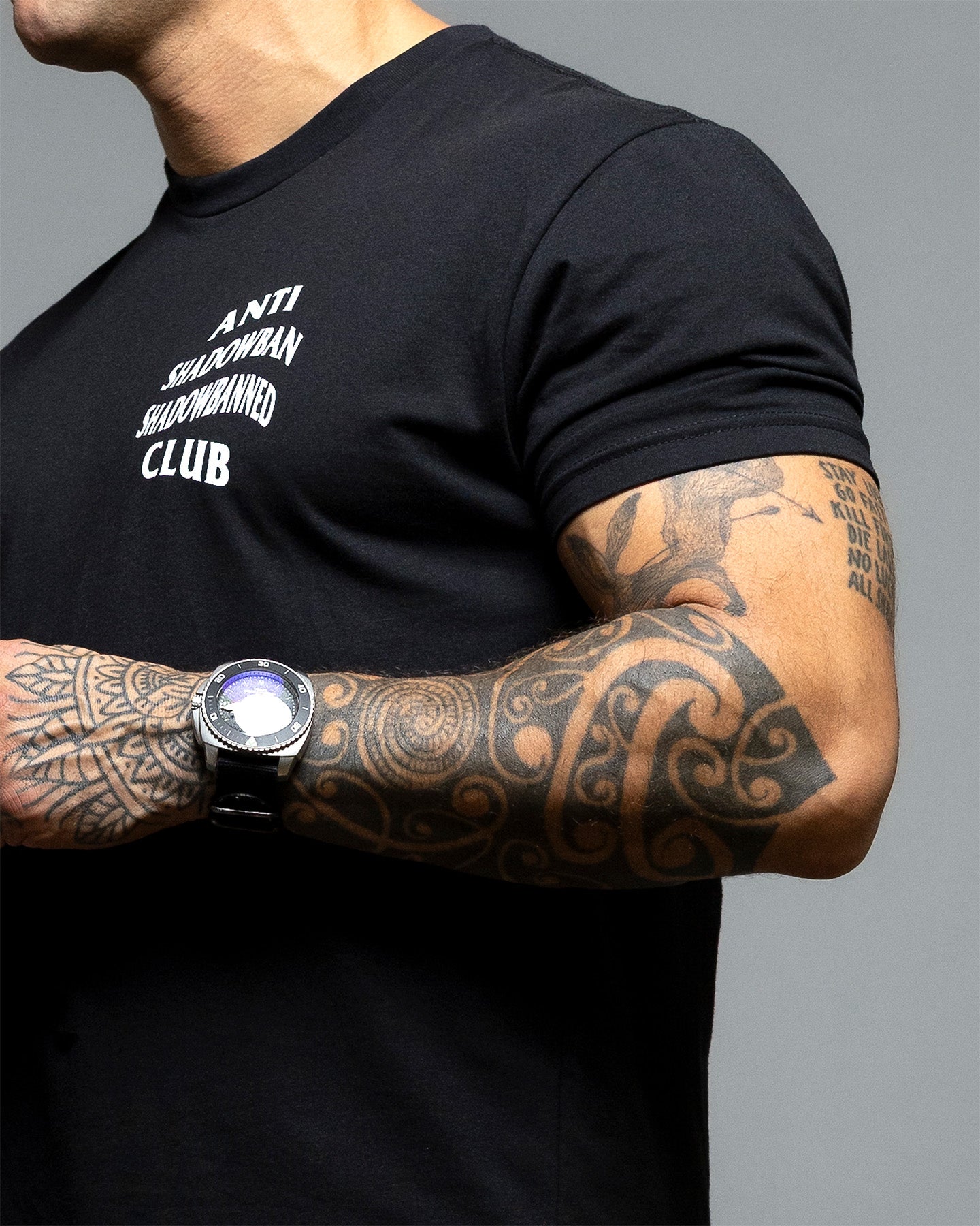 Person wearing a black t-shirt with 'ANTI SHADOWBAN SHADOWBANNED CLUB' text on the front against a gray background. #color_black