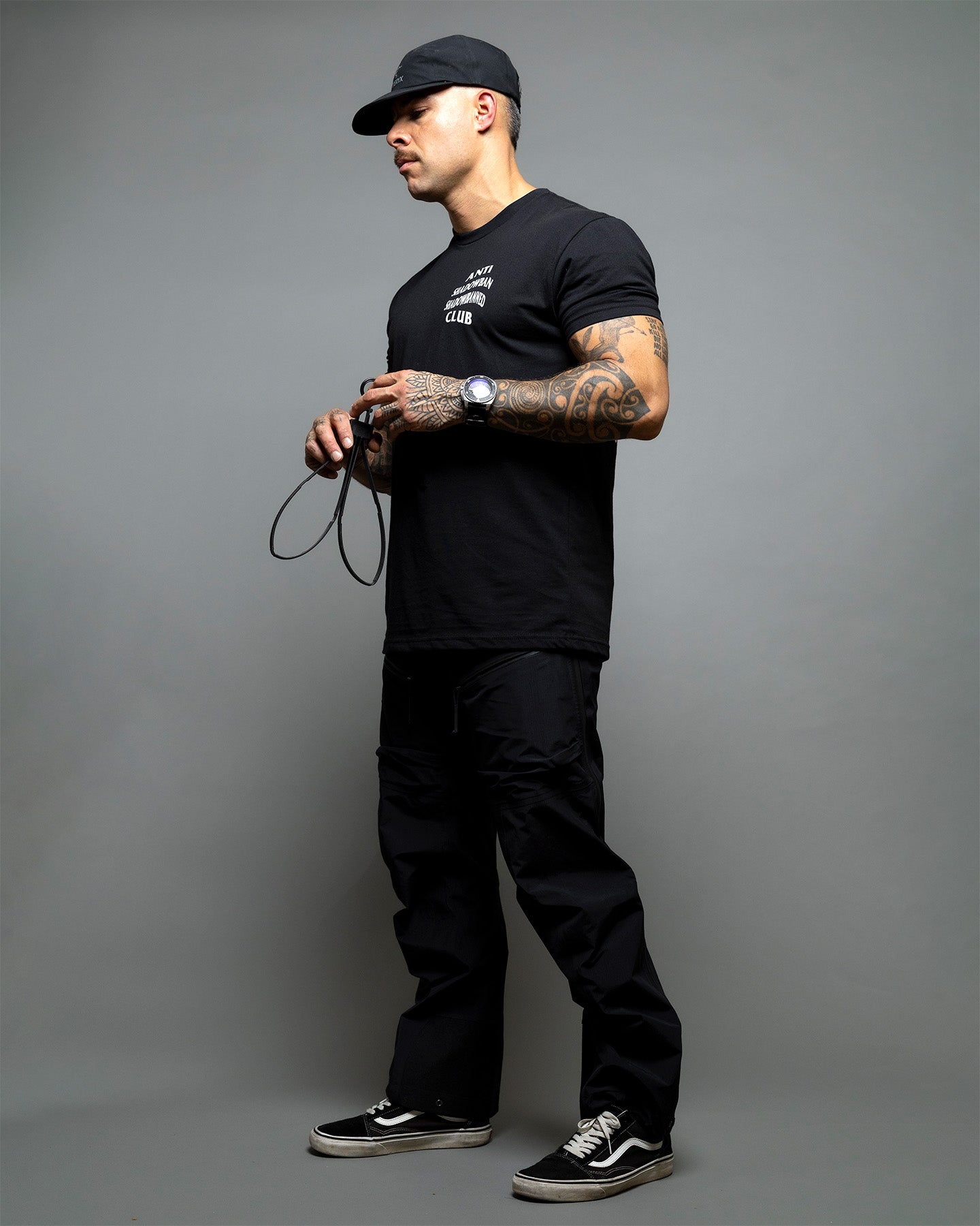 Man wearing a black t-shirt, pants, and cap on a gray background, wearing a black t-shirt with 'ANTI SHADOWBAN SHADOWBANNED CLUB' text on the front. #color_black