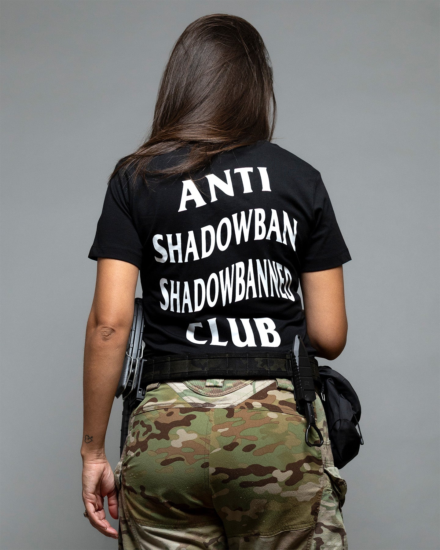 Person wearing a black t-shirt with 'ANTI SHADOWBAN SHADOWBANNERS CLUB' text, standing against a gray background. #color_black
