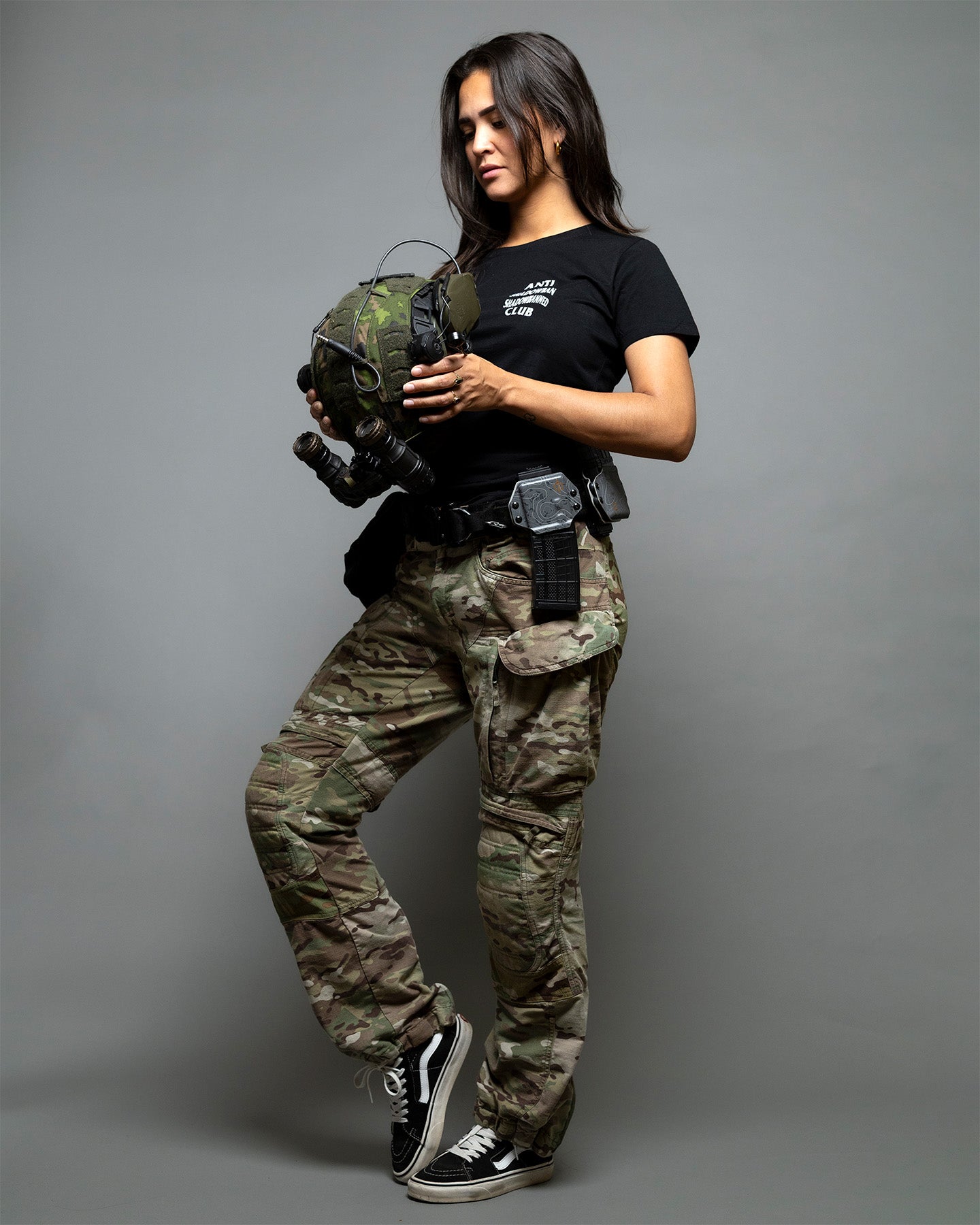Person wearing camouflage pants and a black t-shirt with tactical gear on a gray background. #color_black