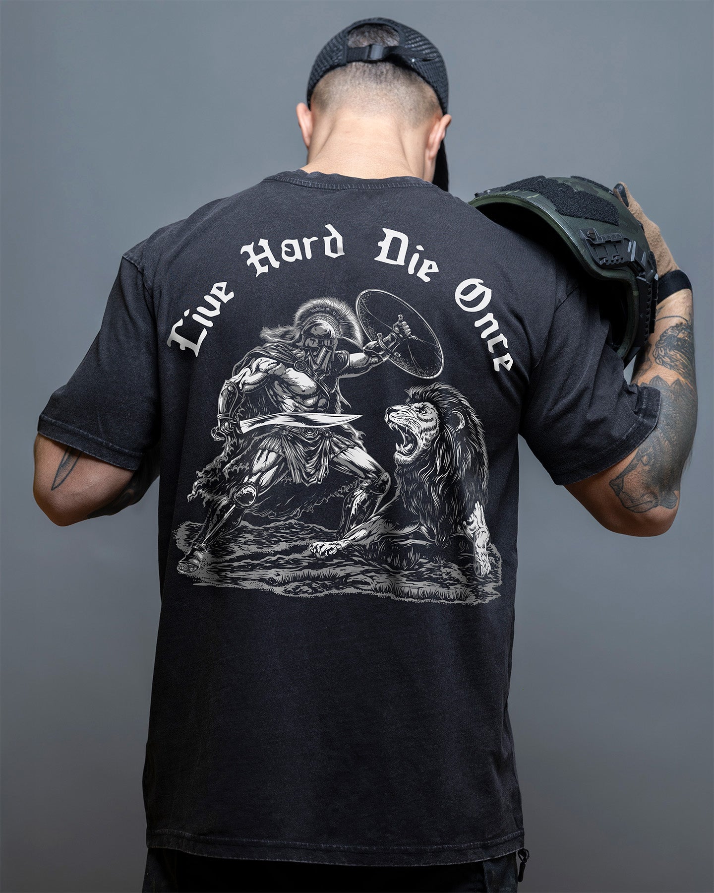 Person wearing a black t-shirt with a graphic design and text on the back, against a gray background. #color_black