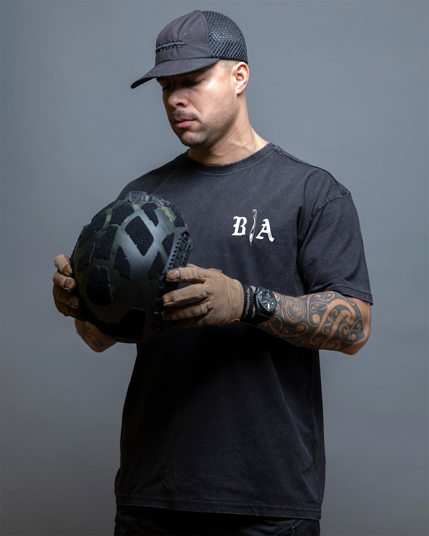 Man holding a helmet wearing a black t-shirt with 'BIA' logo on a gray background. #color_black