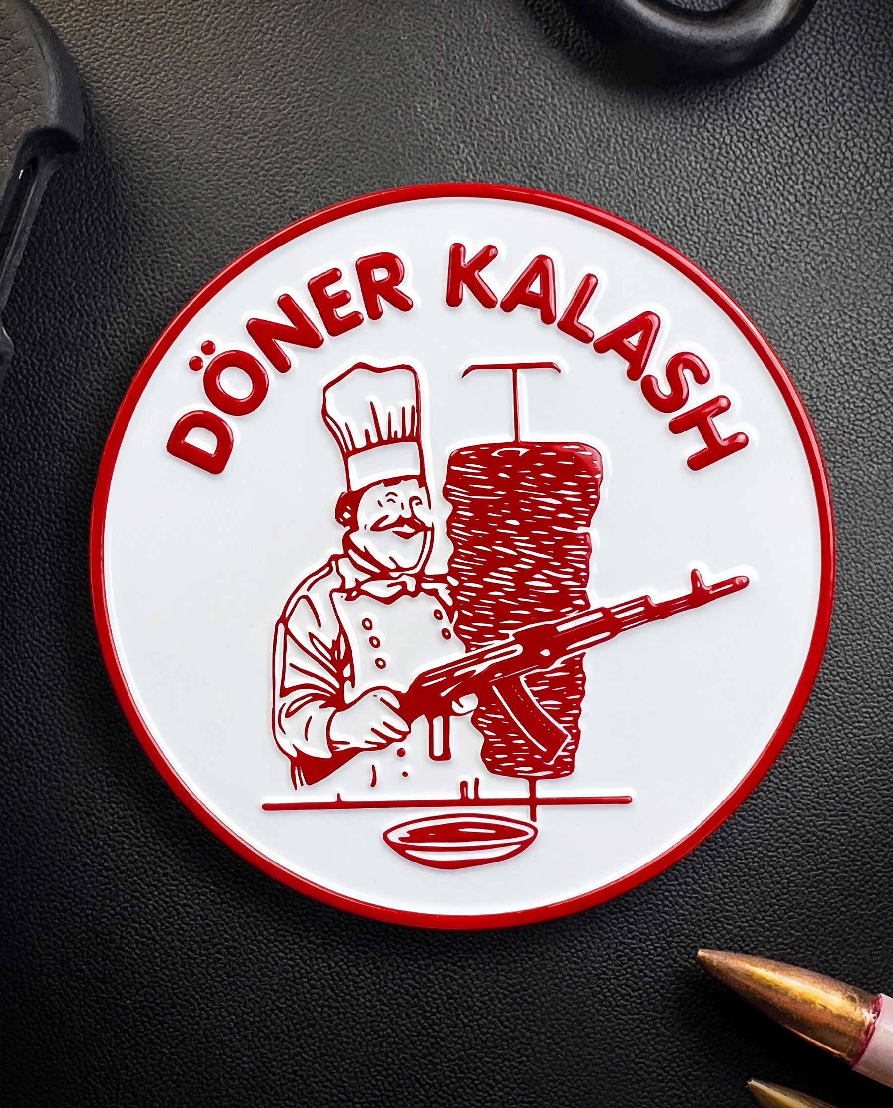 Circular Coin with a Döner Kebab chef and rifle on a dark surface, with the text "Döner Kalash"