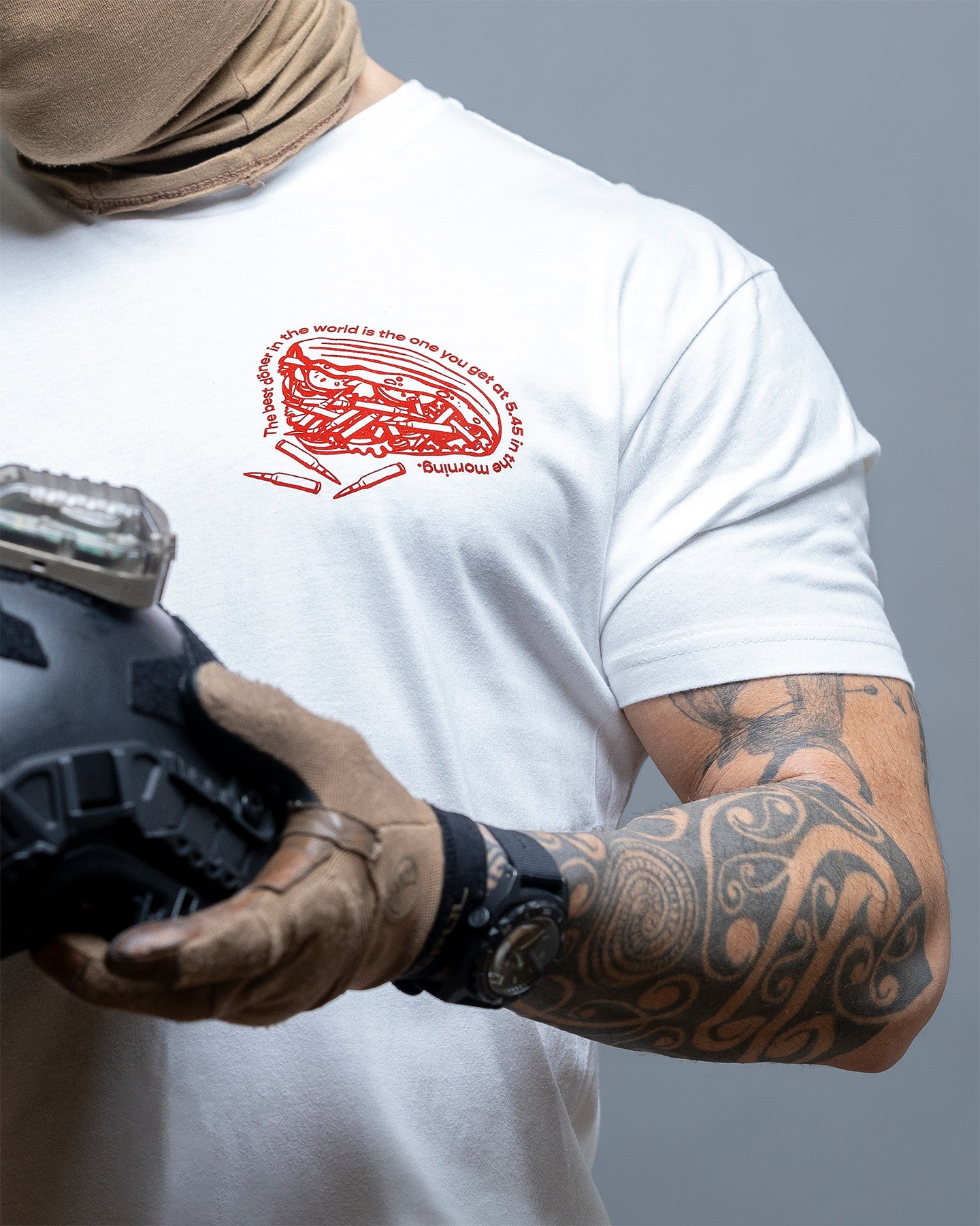 Person wearing a white t-shirt with a red logo, holding a helmet against a gray background. #color_white