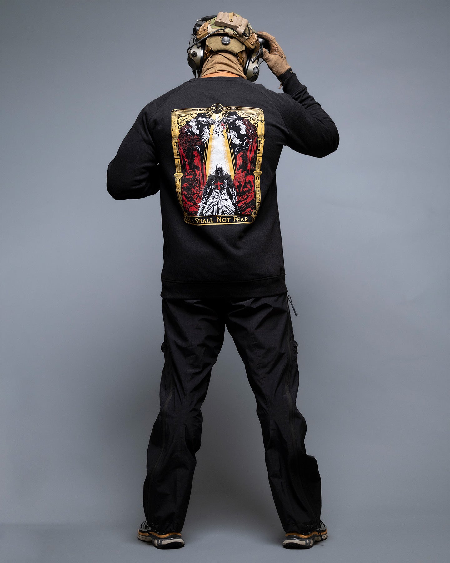 Person wearing a black sweatshirt with a graphic design on the back against a gray background. #color_black