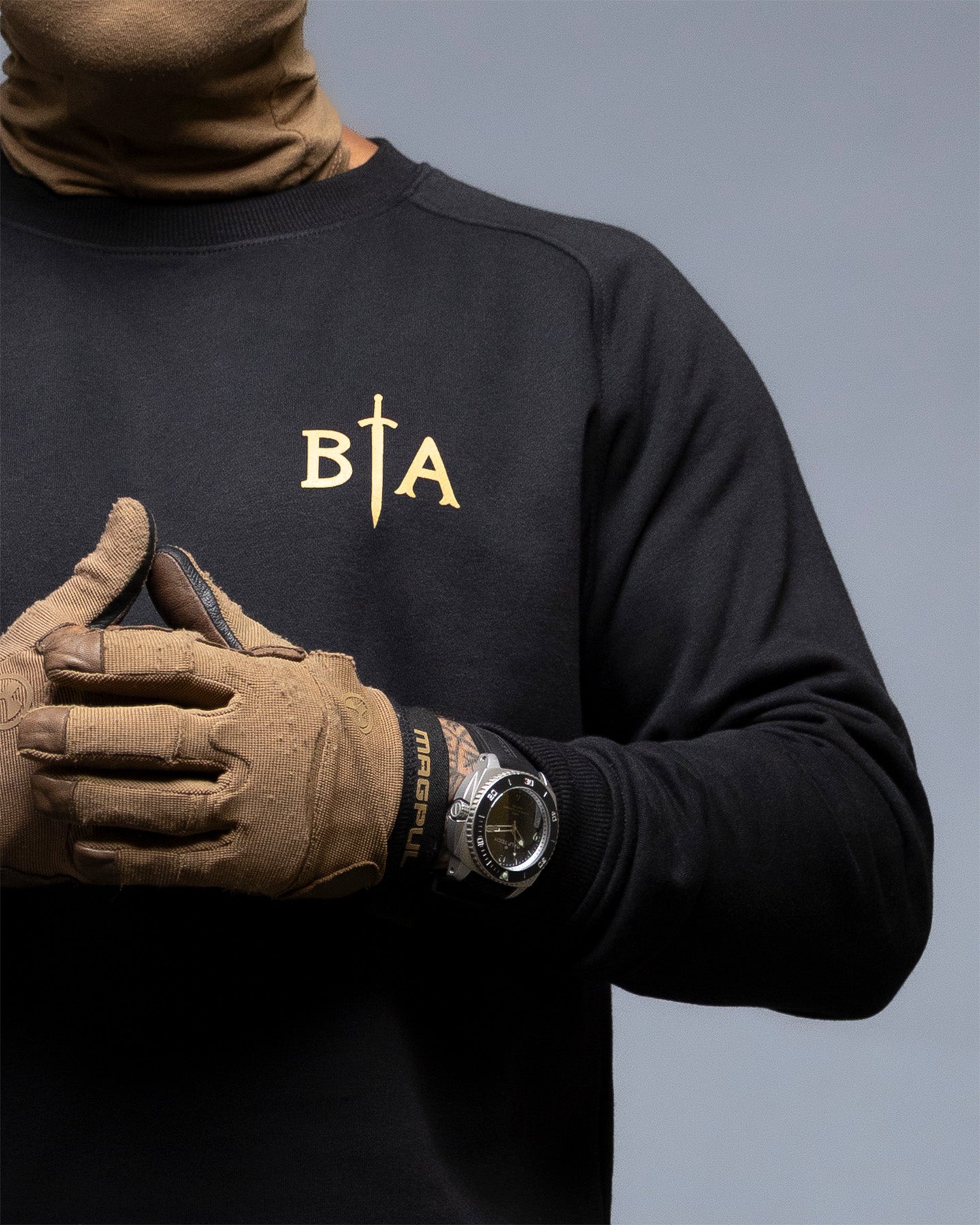 Person wearing a black sweatshirt with 'BIA' logo, brown gloves, and a watch on a gray background. #color_black