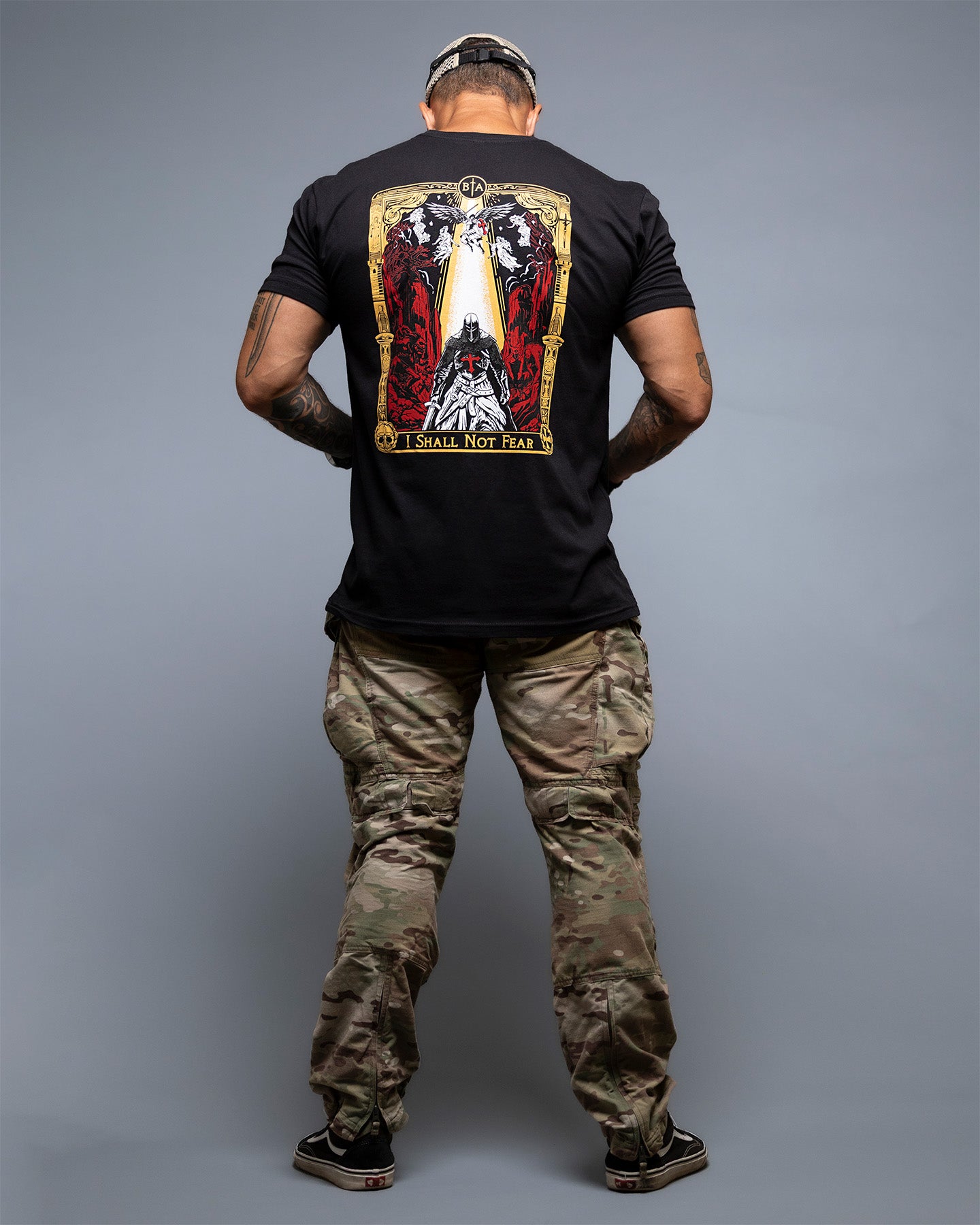 Person wearing a black t-shirt with a graphic design on the back, standing against a gray background. #color_black