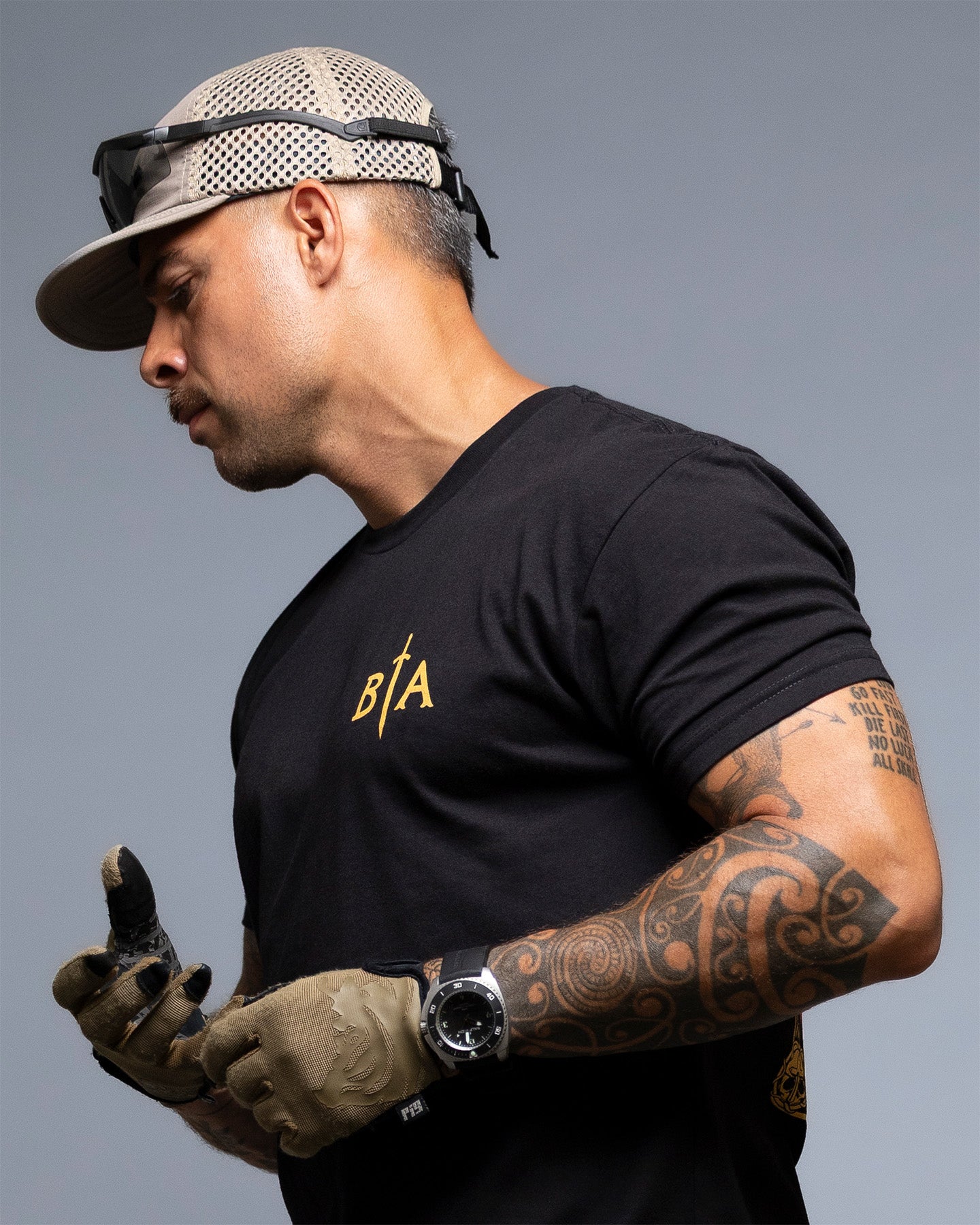 Man wearing a black t-shirt with 'BIA' logo, gloves, and cap on a gray background. #color_black