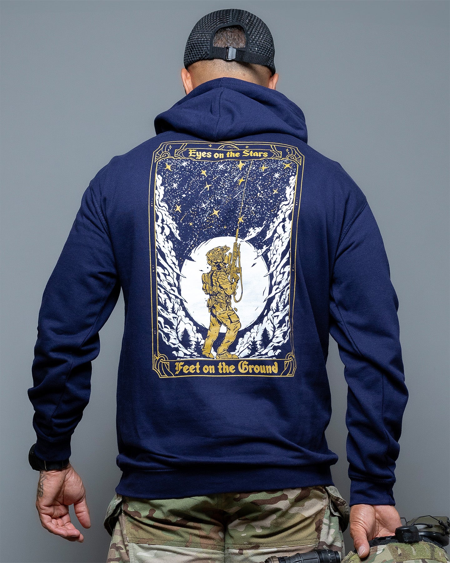 Person wearing a navy blue hoodie with a celestial design on the back, standing against a gray background. #color_navy