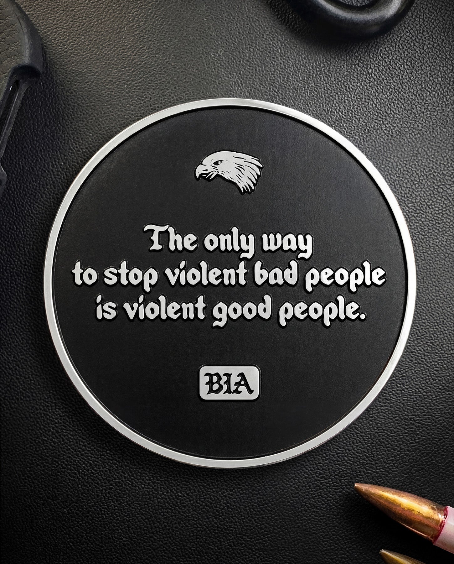 Circular metal Coin with the text "They only way to stop violent bad people is violent good people" and the "BIA" logo on a black surface