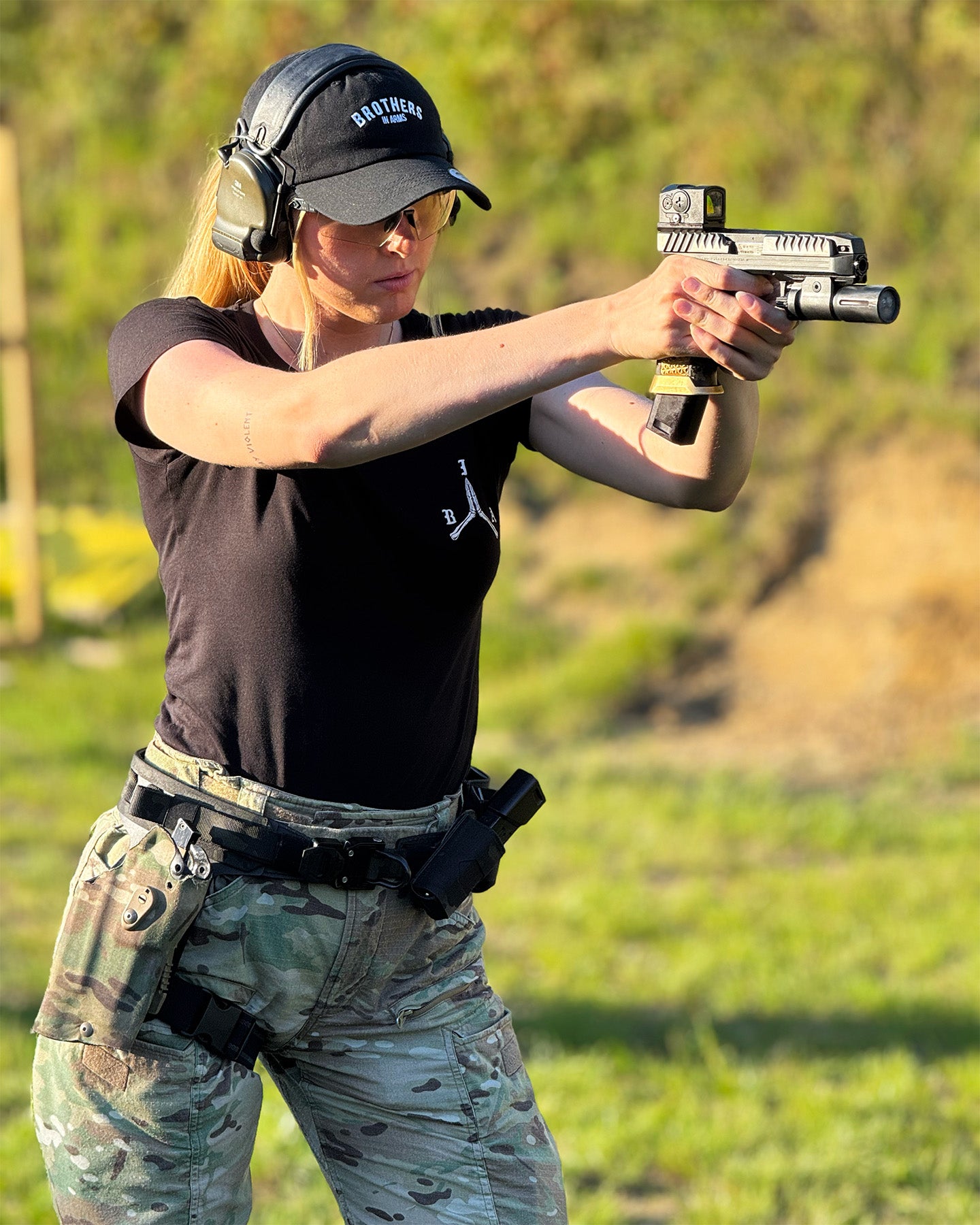 Person in tactical gear holding a firearm in an outdoor setting. #color_black #in_field