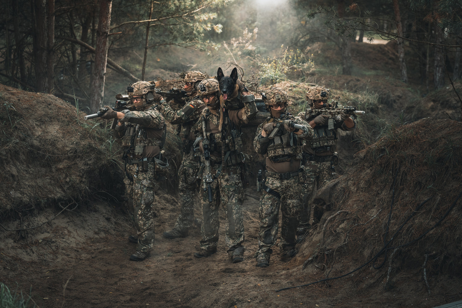 Soldiers looking like a special forces unit walking through a forest with their arms out.
