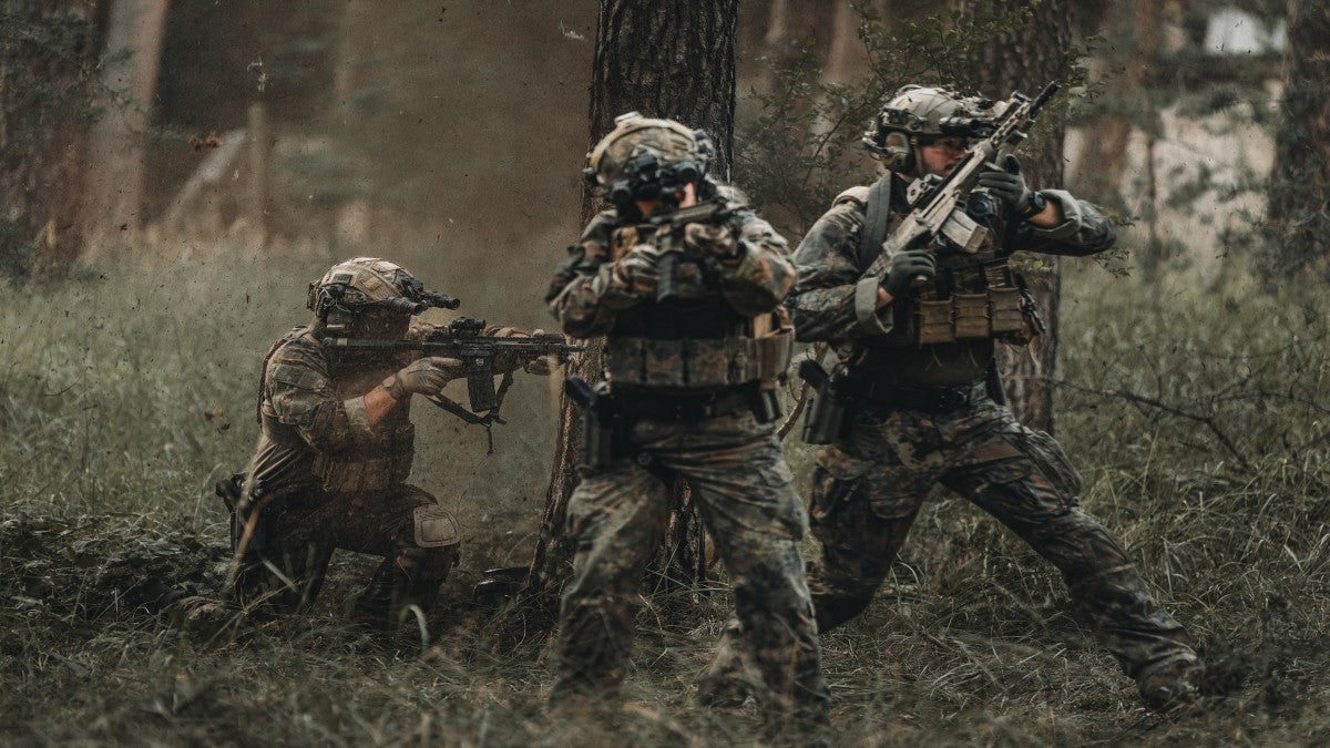Soldiers in military clothing walking through a forest. 