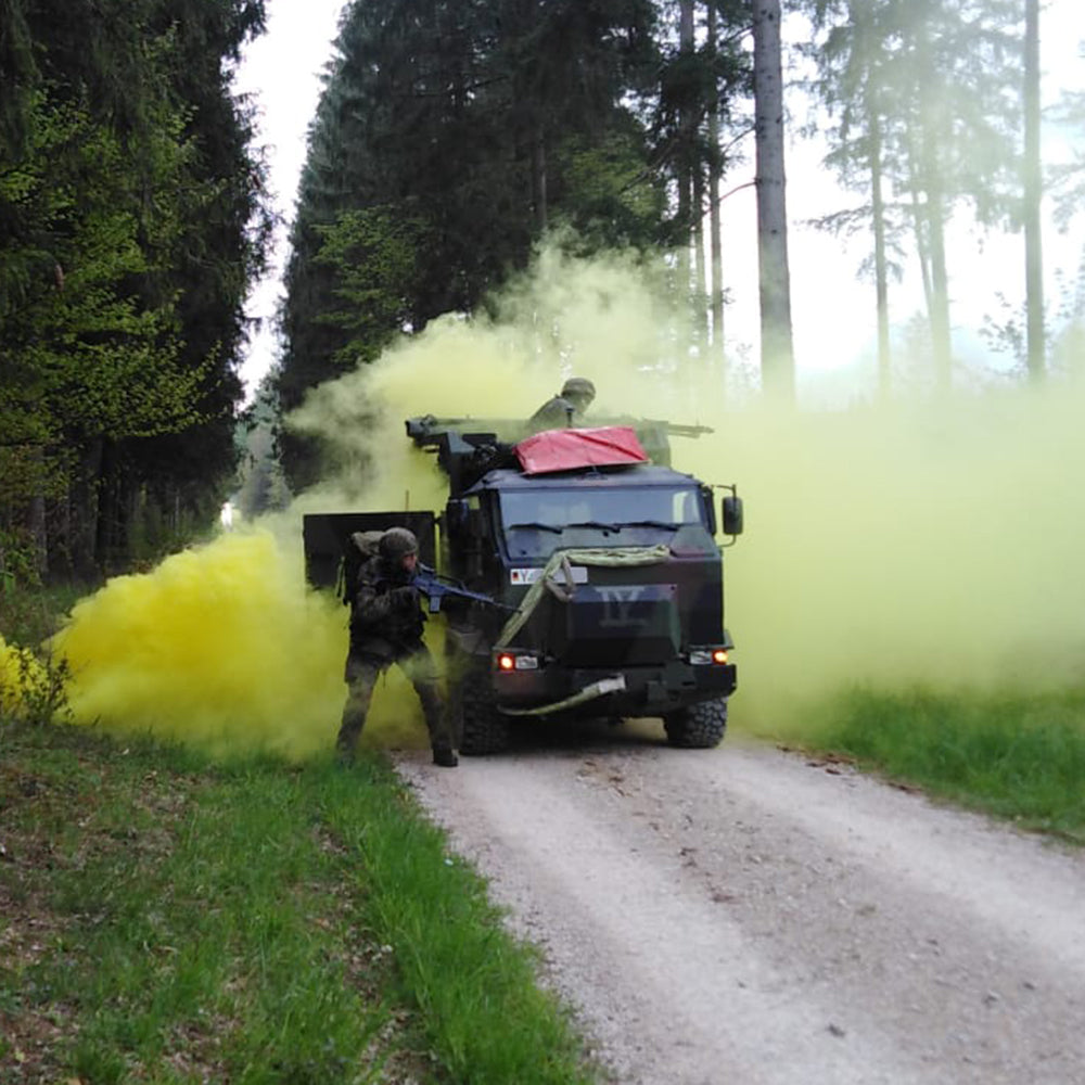 Soldier beside an armoured vehicle on a forest track in yellow smoke