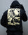 Person wearing a black hoodie with a graphic design on the back against a gray background - Acta Non Verba Hoodie