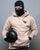 Person wearing a beige hoodie with text, black balaclava, and holding a helmet against a gray background - Acta Non Verba Hoodie