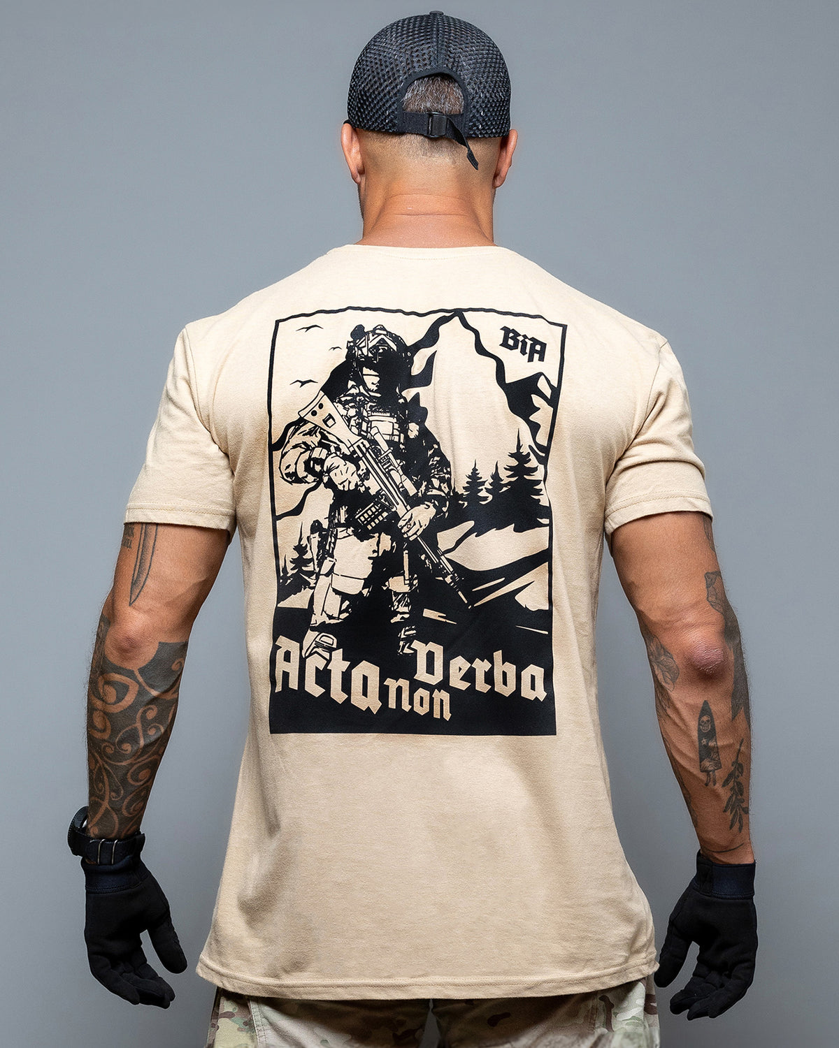 Rear view of the sand Acta Non Verba T-Shirt with the large soldier and mountain print