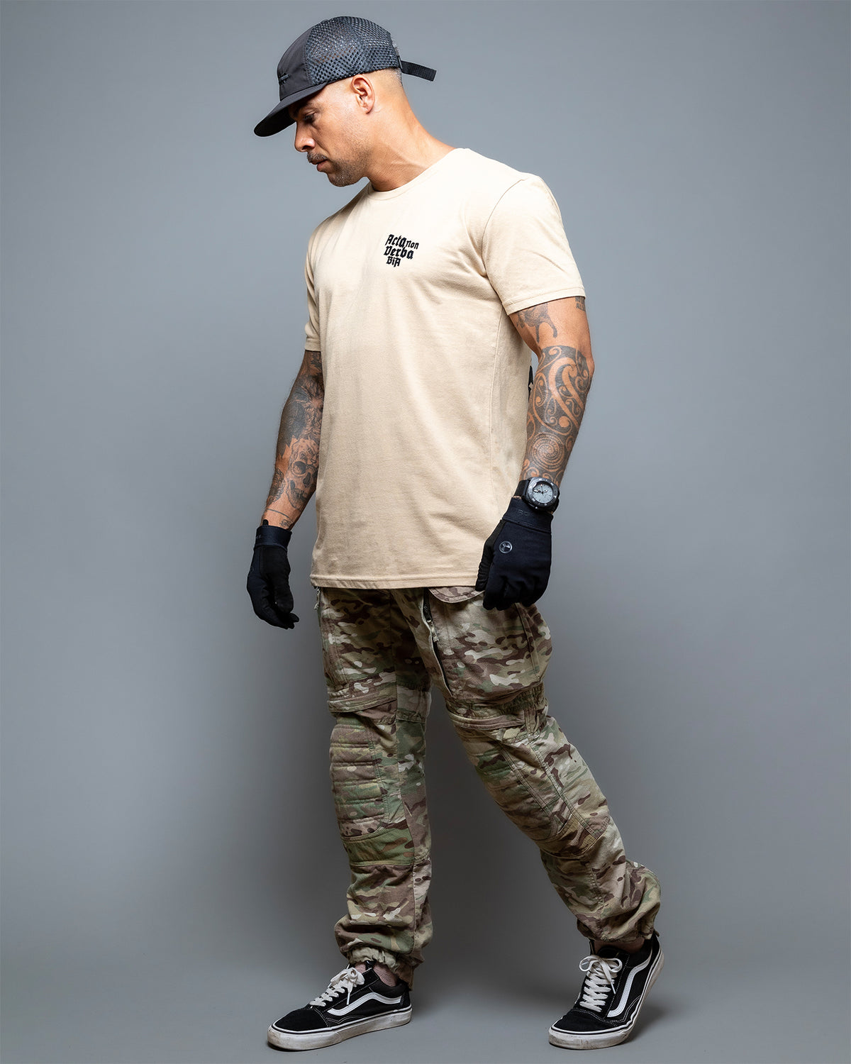 Full-length shot of the sand Acta Non Verba T-Shirt worn with camo trousers