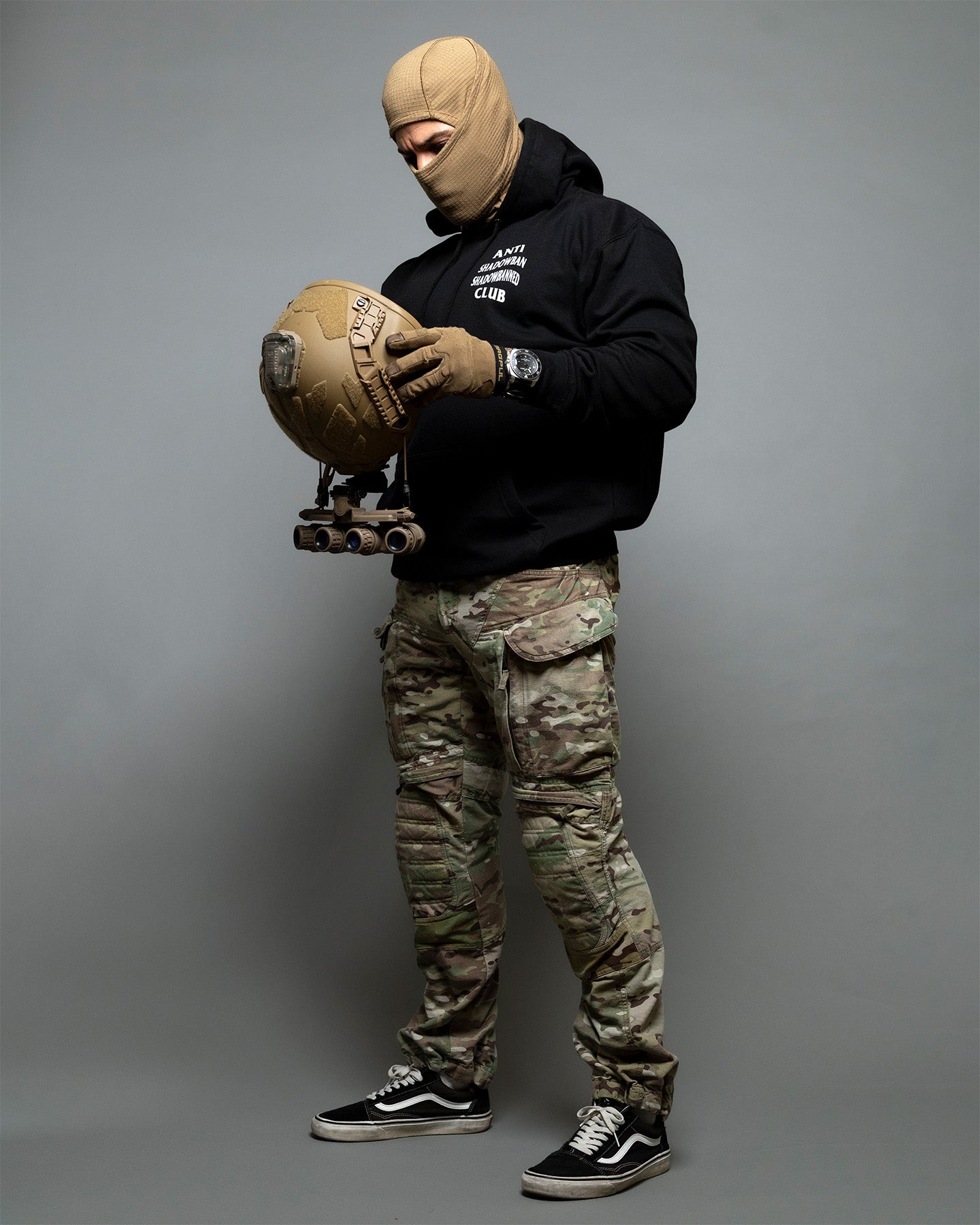 Person wearing a black hoodie and camouflage pants holding a ball against a gray background. #color_black
