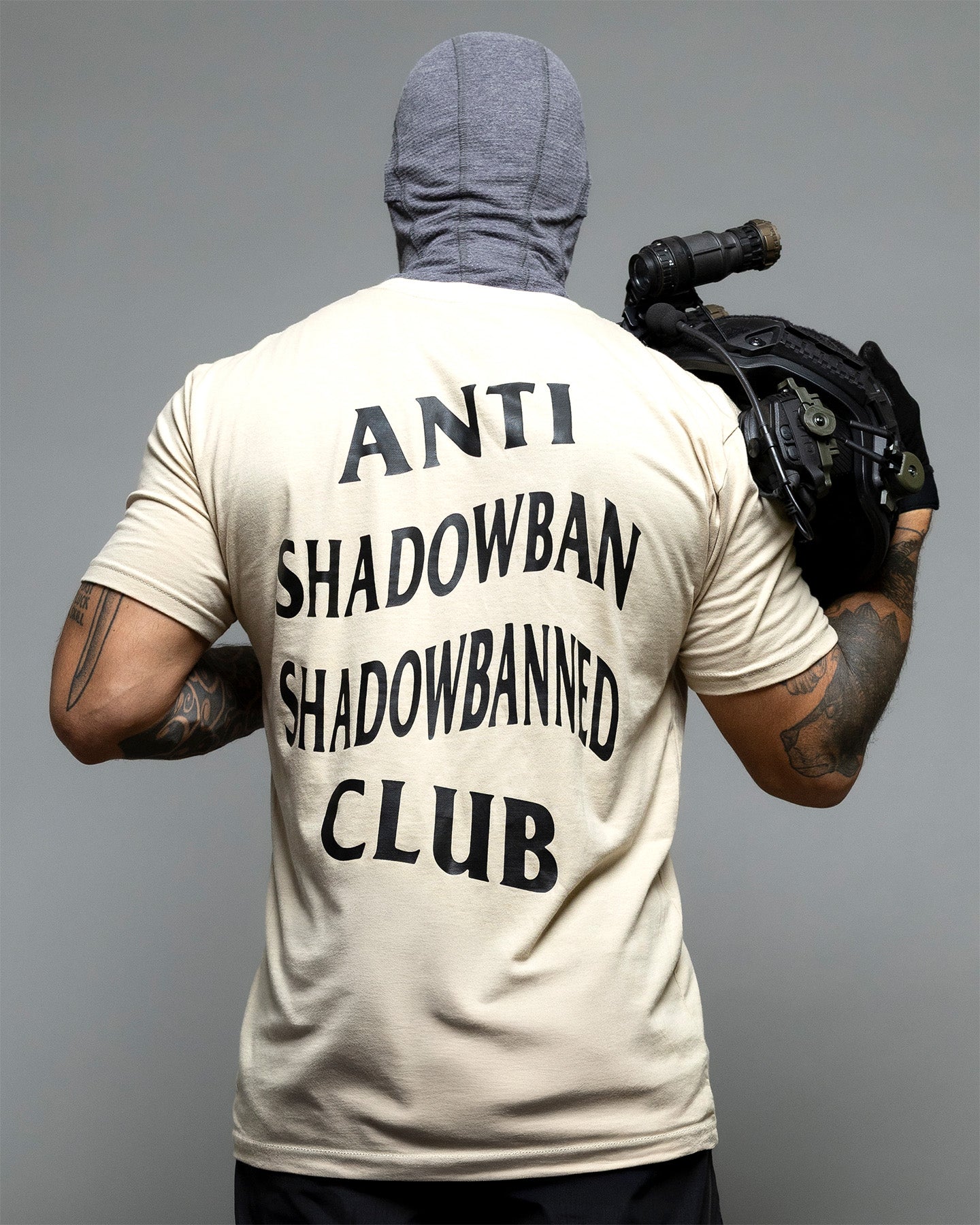 Person wearing a t-shirt with 'ANTI SHADOWBAN SHADOWBANNED CLUB' text on the back, holding a backpack. #color_sand