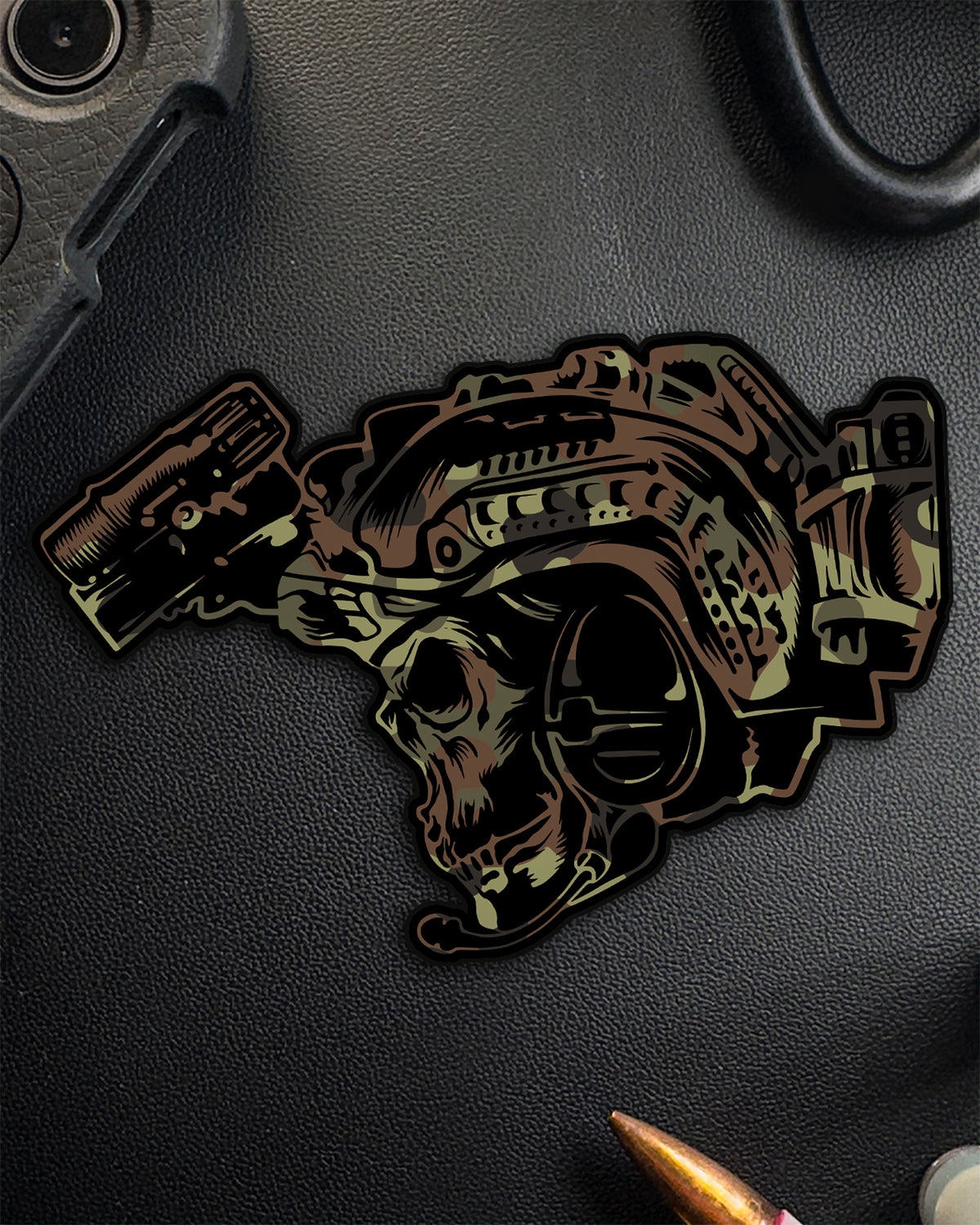 BIA skull sticker in Flecktarn camo on a dark surface next to a rifle cartridge