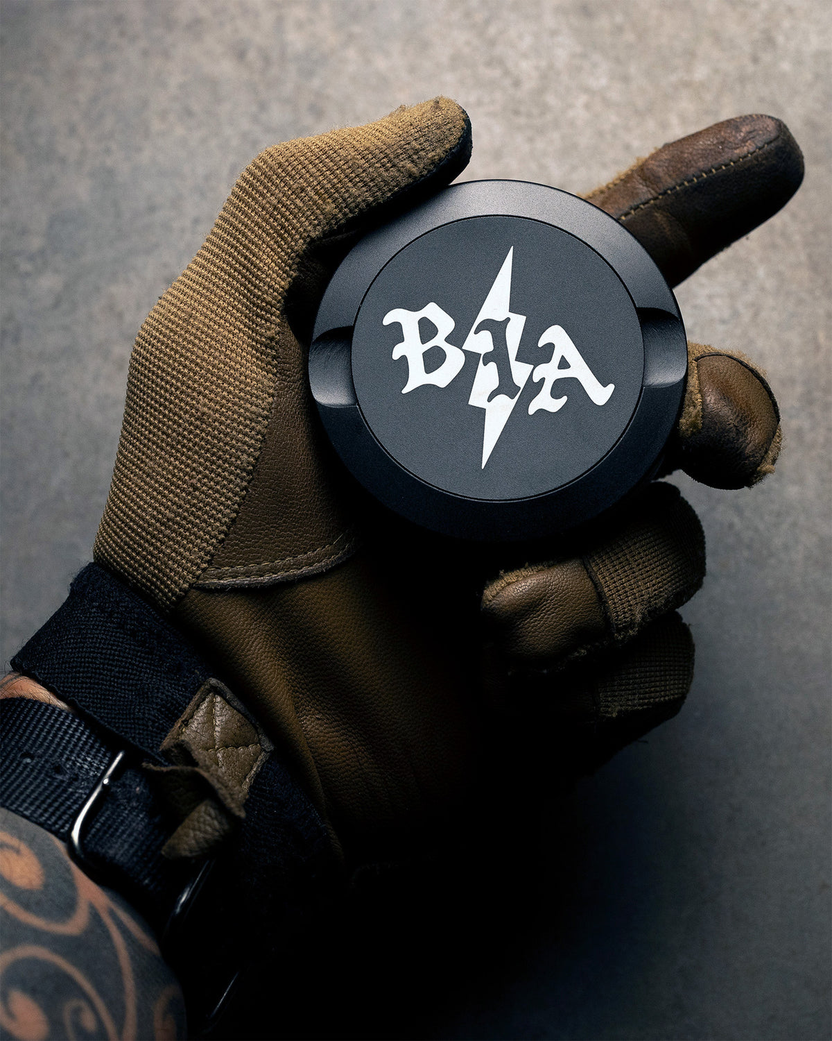 Black Bolt Pouch Can with the Brothers in Arms logo on the lid, held in a brown tactical glove