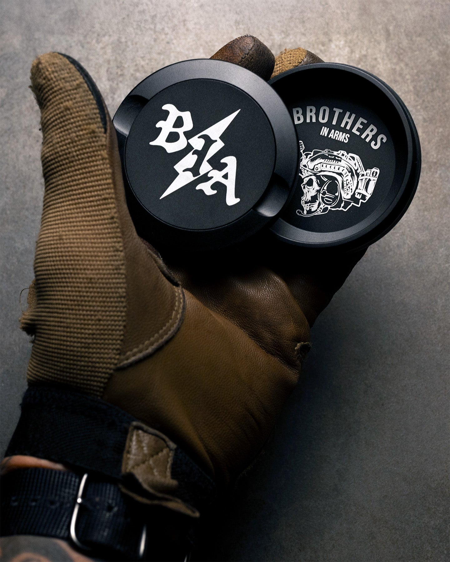 Black push cans with branding held in a brown glove against a gray background. #in_field