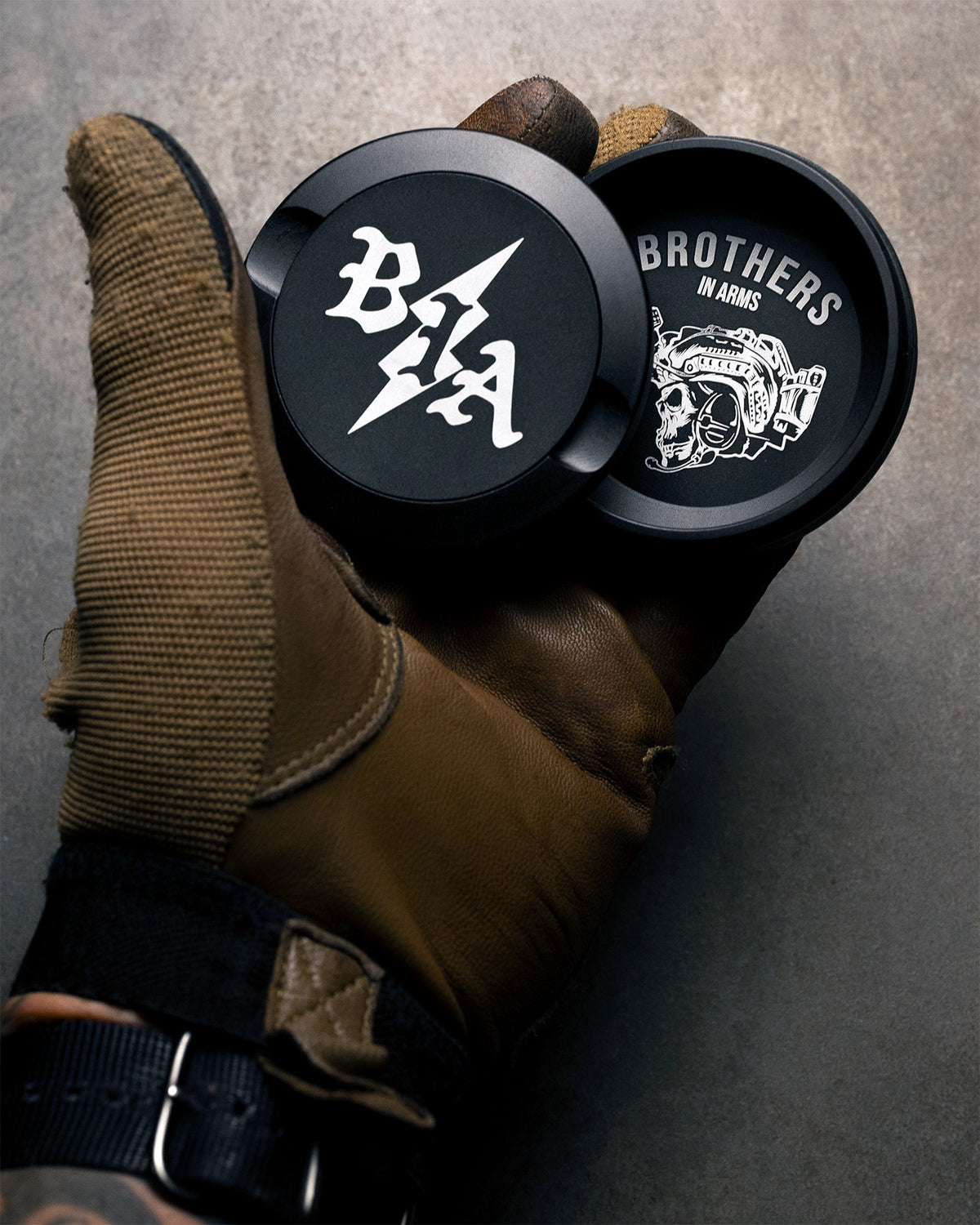 Two black Bolt Pouch Cans held in a brown glove, one showing the logo lid, one the skull artwork