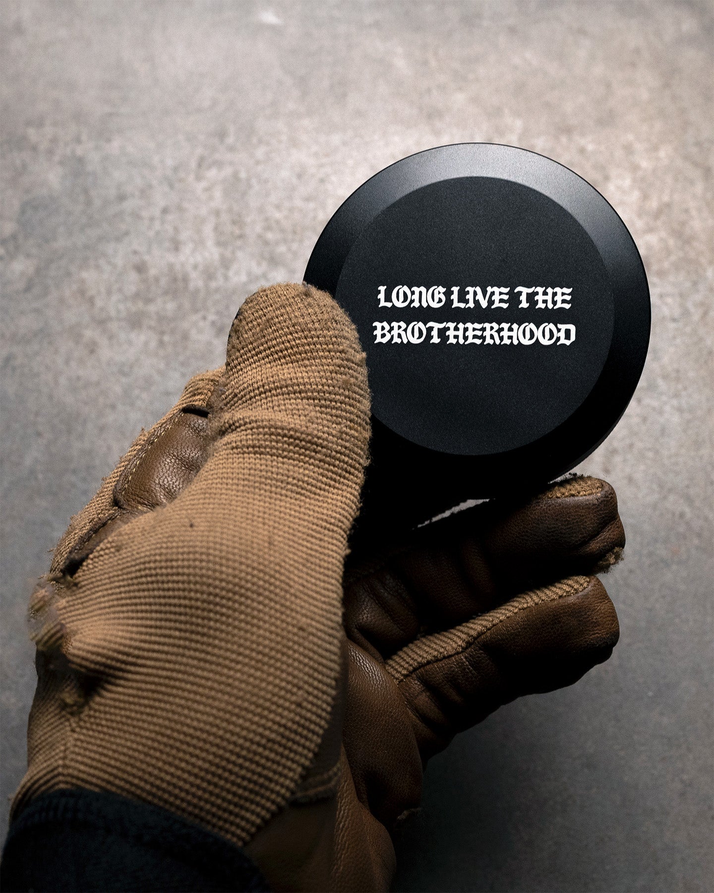 Hand wearing a brown glove holding a pouch can with 'Long Live the Brotherhood' text on a gray background. #in_field
