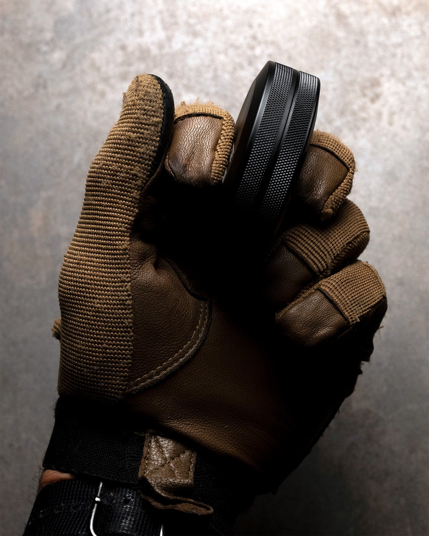 Brown tactical glove with black Pouch Can on a textured gray background. #in_field