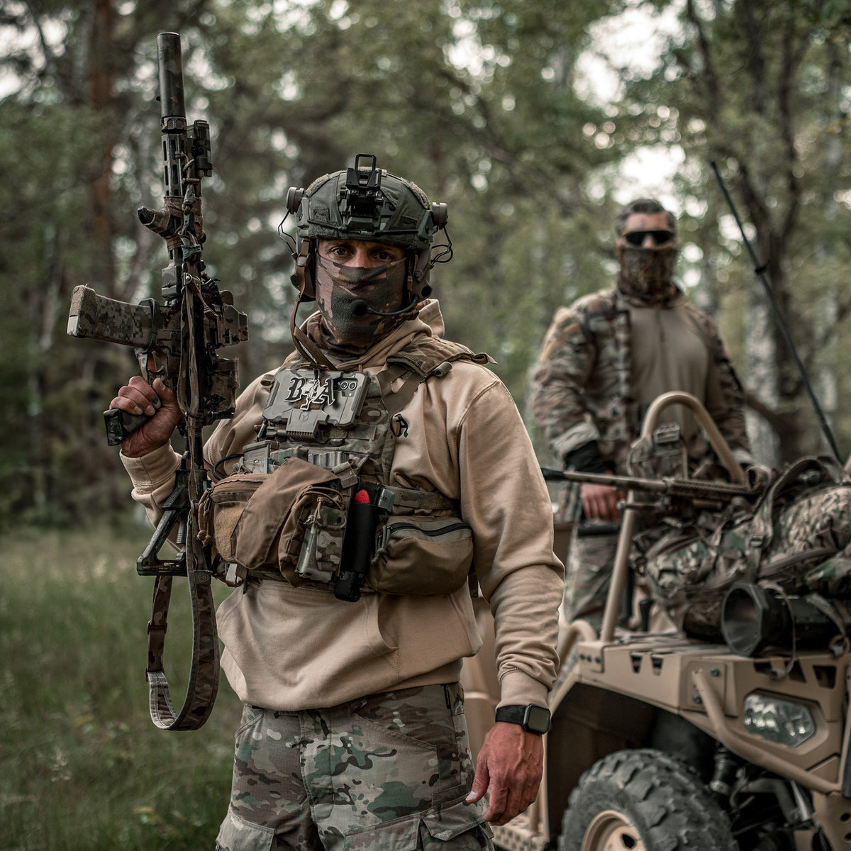 Two soldiers in full kit with rifles standing next to a vehicle in the woods