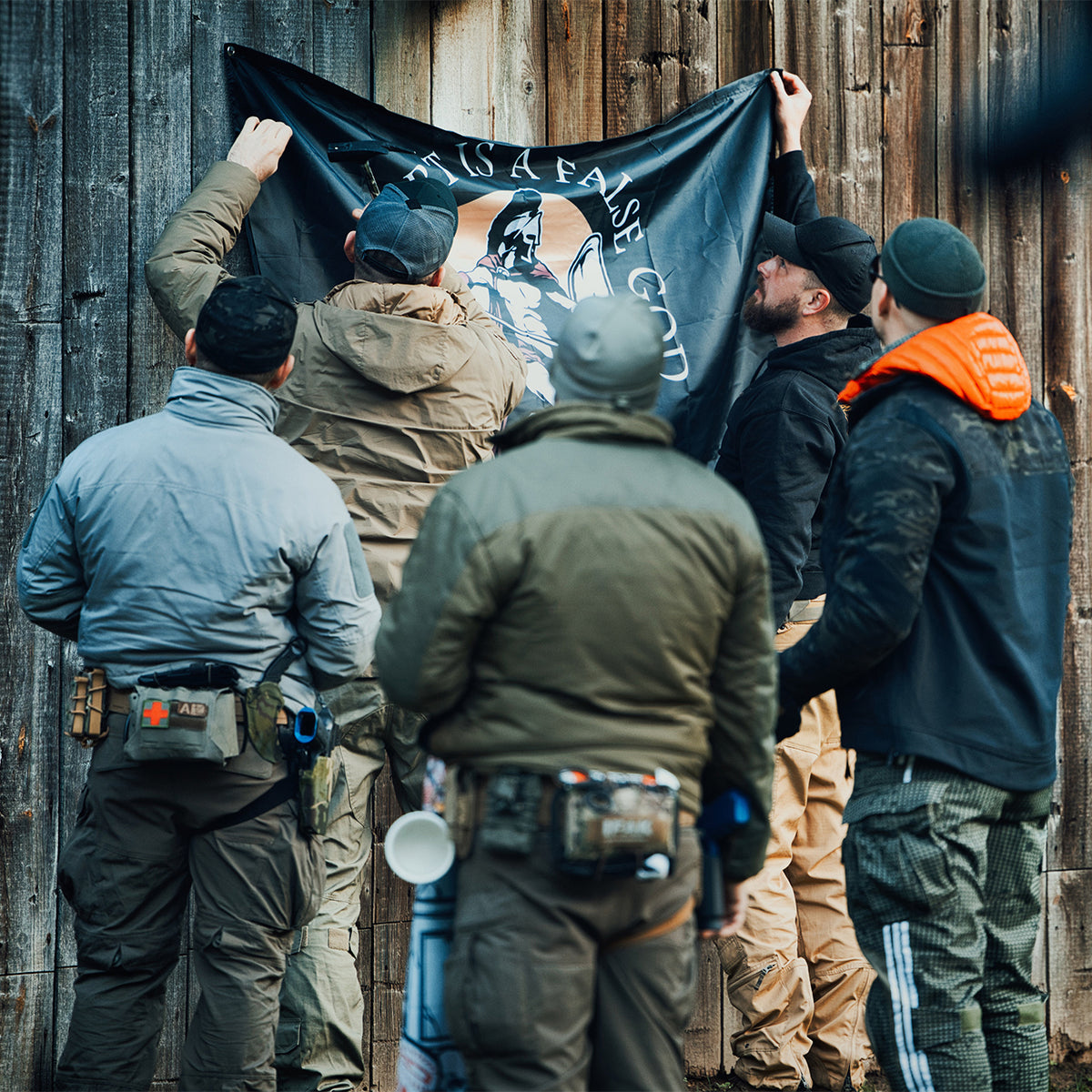 Group of men mounting the Comfort Is A False God flag on a wooden wall