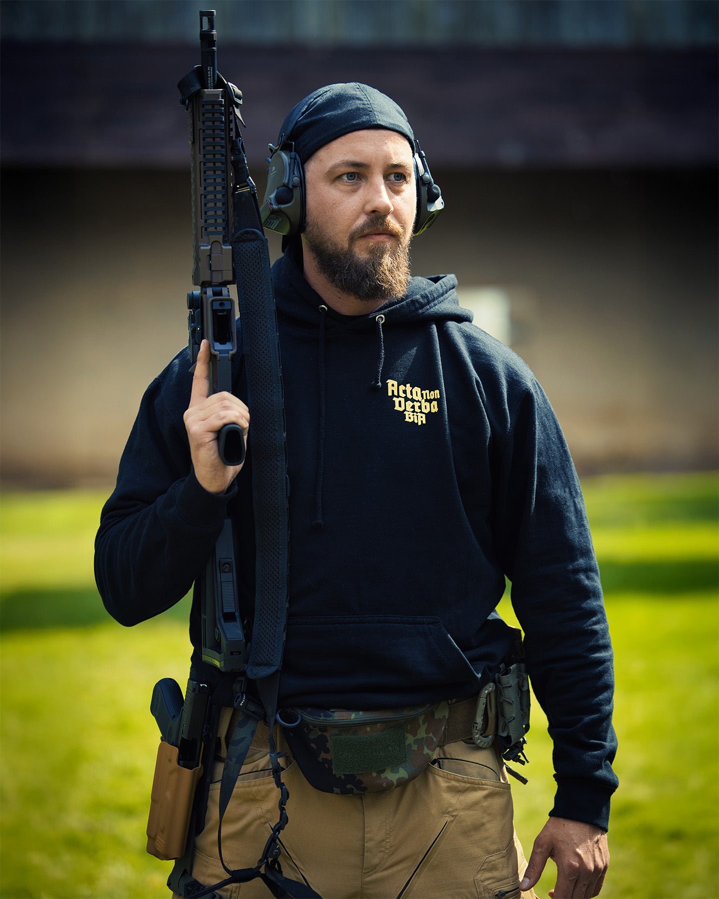 Man holding a rifle in an outdoor setting - Acta Non Verba Hoodie 