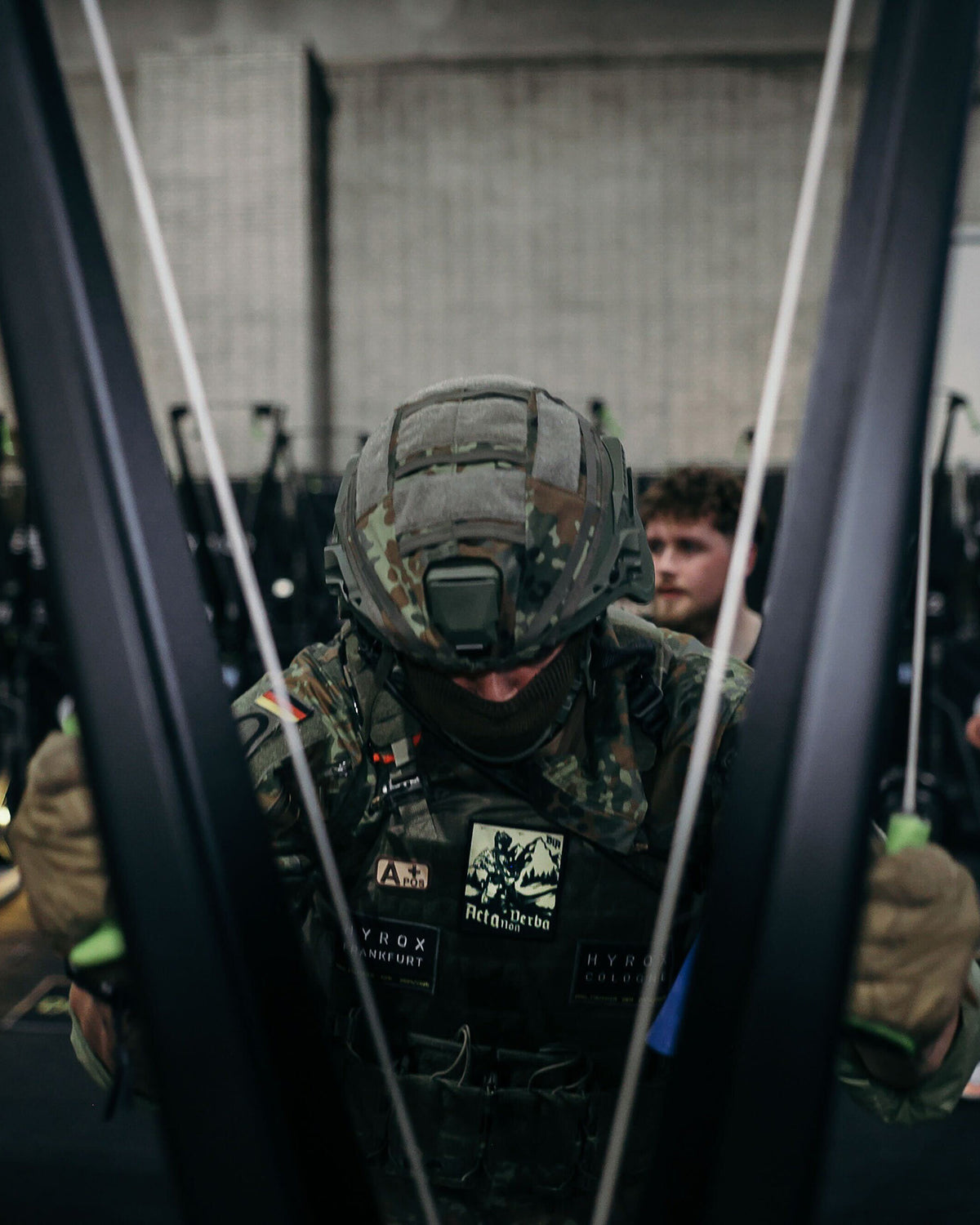 Soldier in full kit and helmet at an indoor competition, patches on his plate carrier