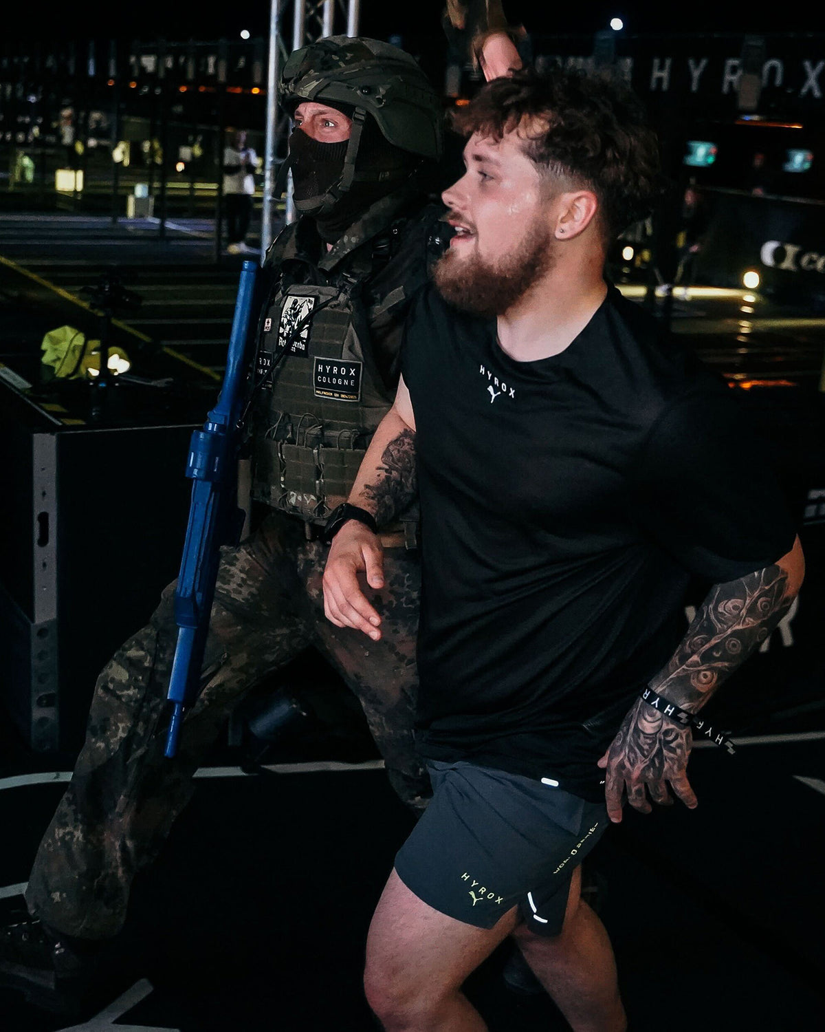Soldier in kit and an athlete in a black shirt running side by side at night