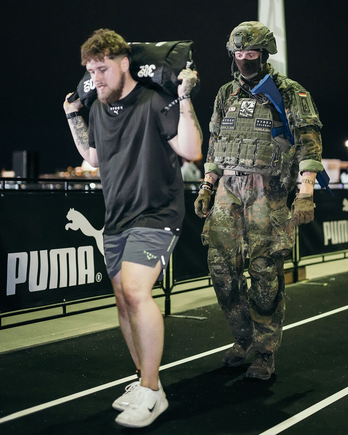 Athlete on a running track drinking beside a soldier in full kit and helmet