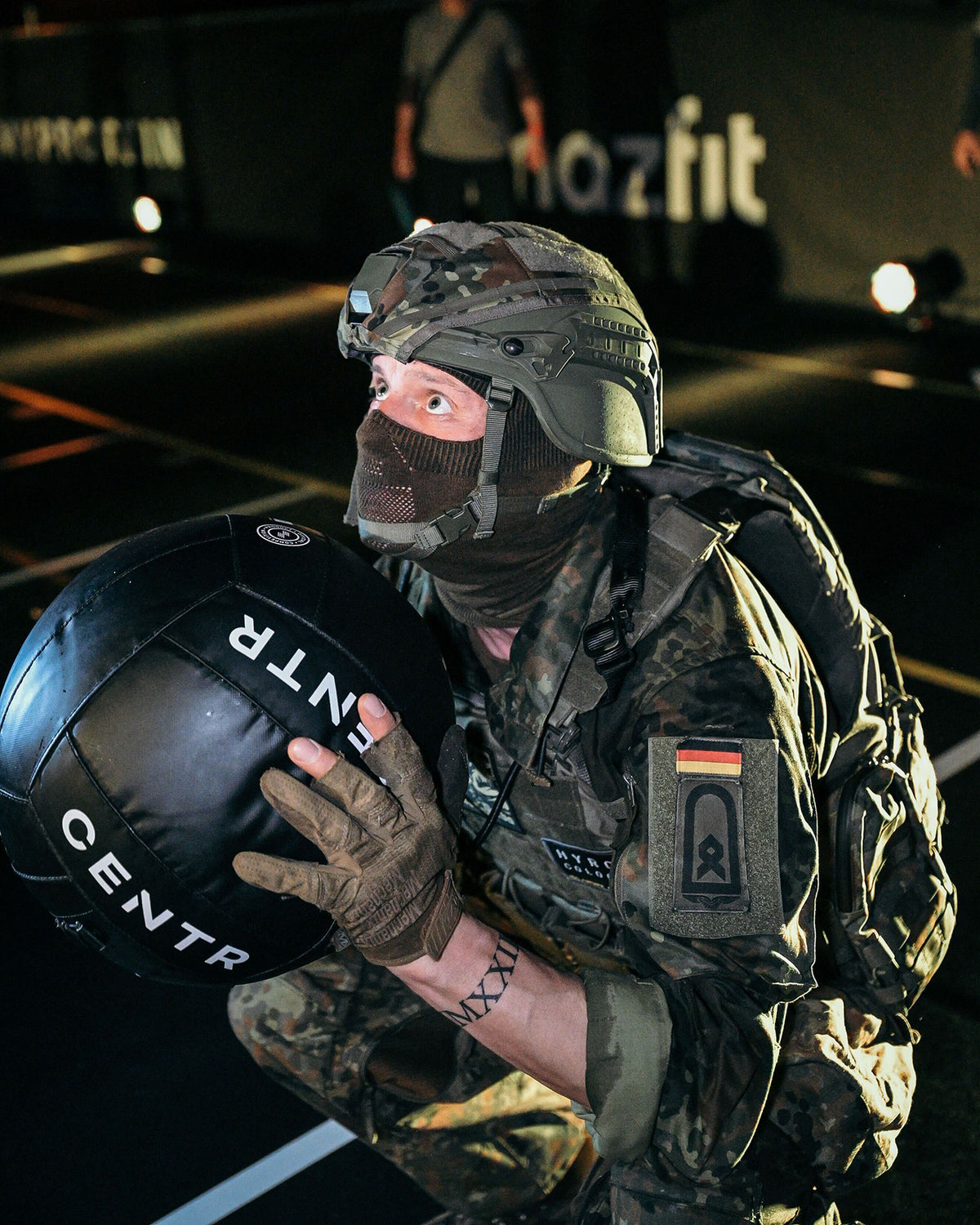 Soldier kneeling in helmet and face mask, gear and patches on his plate carrier