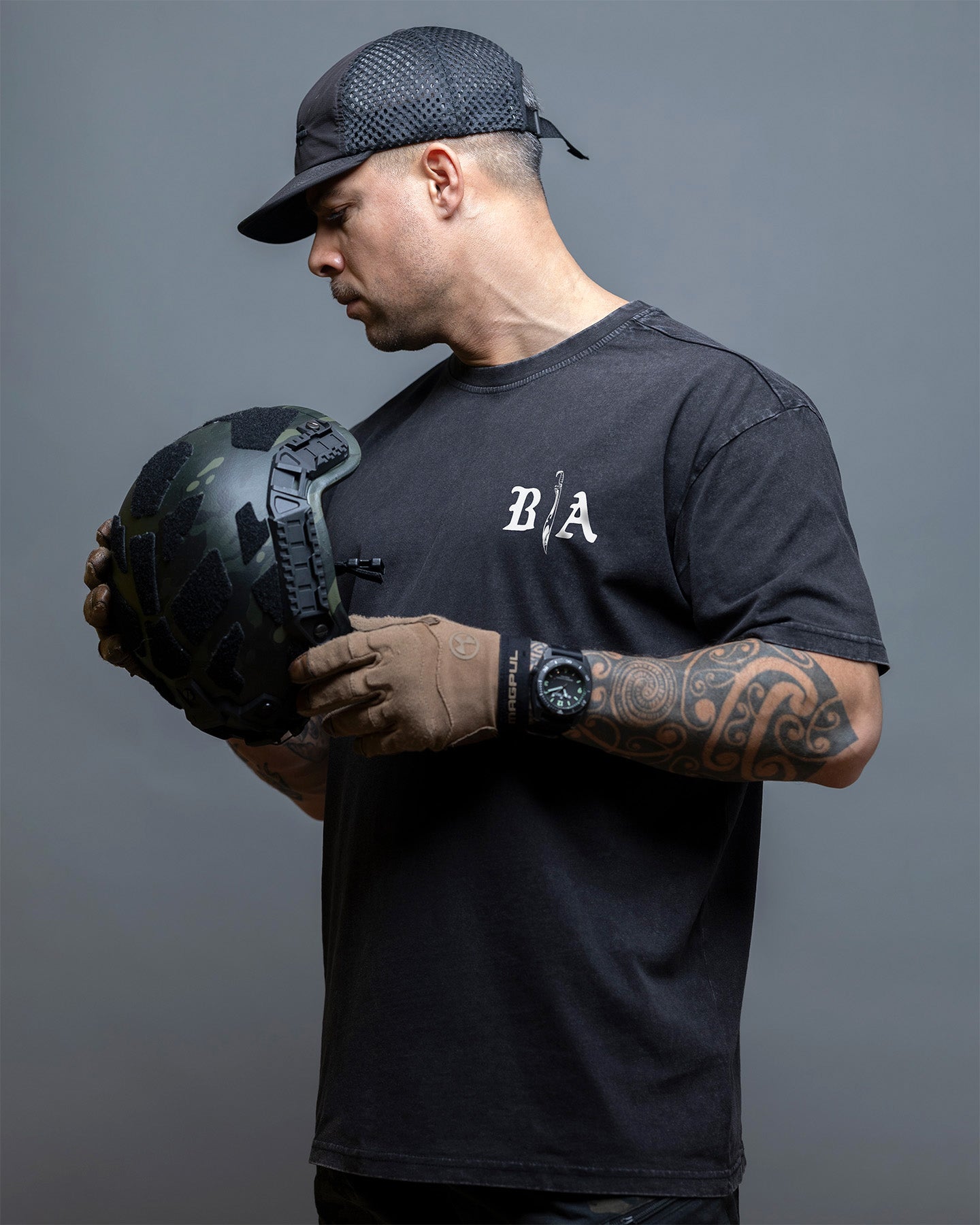 Man holding a black helmet wearing a black t-shirt with a logo, on a gray background. #color_black