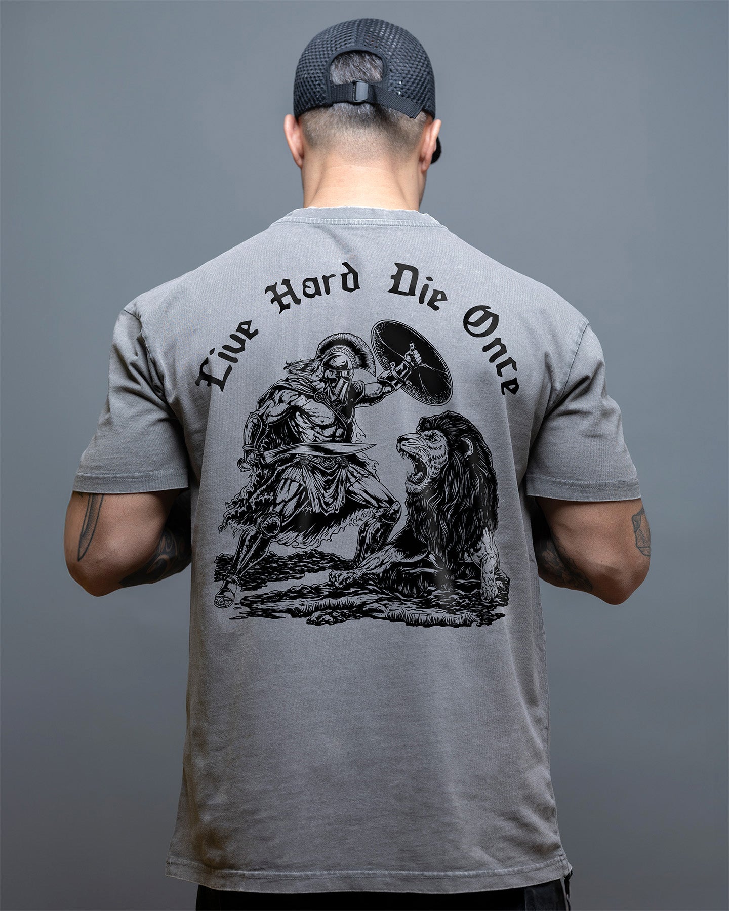 Man wearing a gray t-shirt with a graphic design and text on the back against a gray background. #color_gray