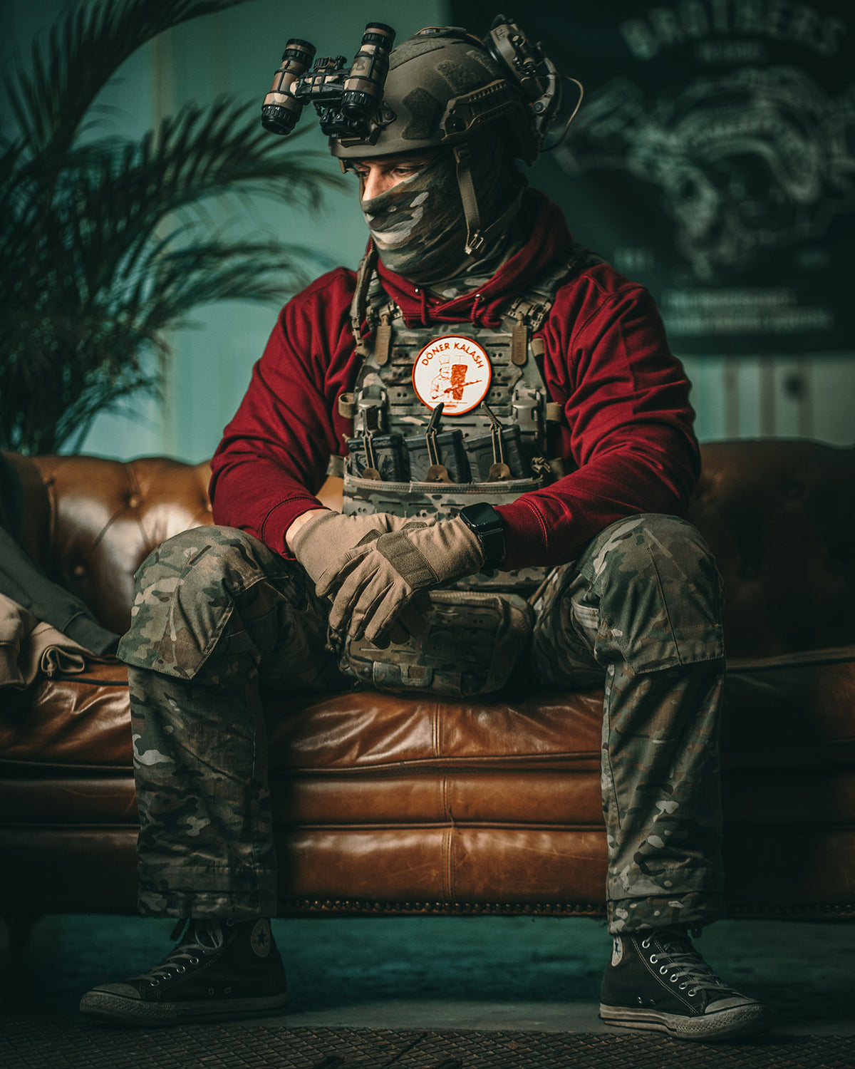 Soldier in kit seated on a leather couch, the Döner Kalash patch on his chest