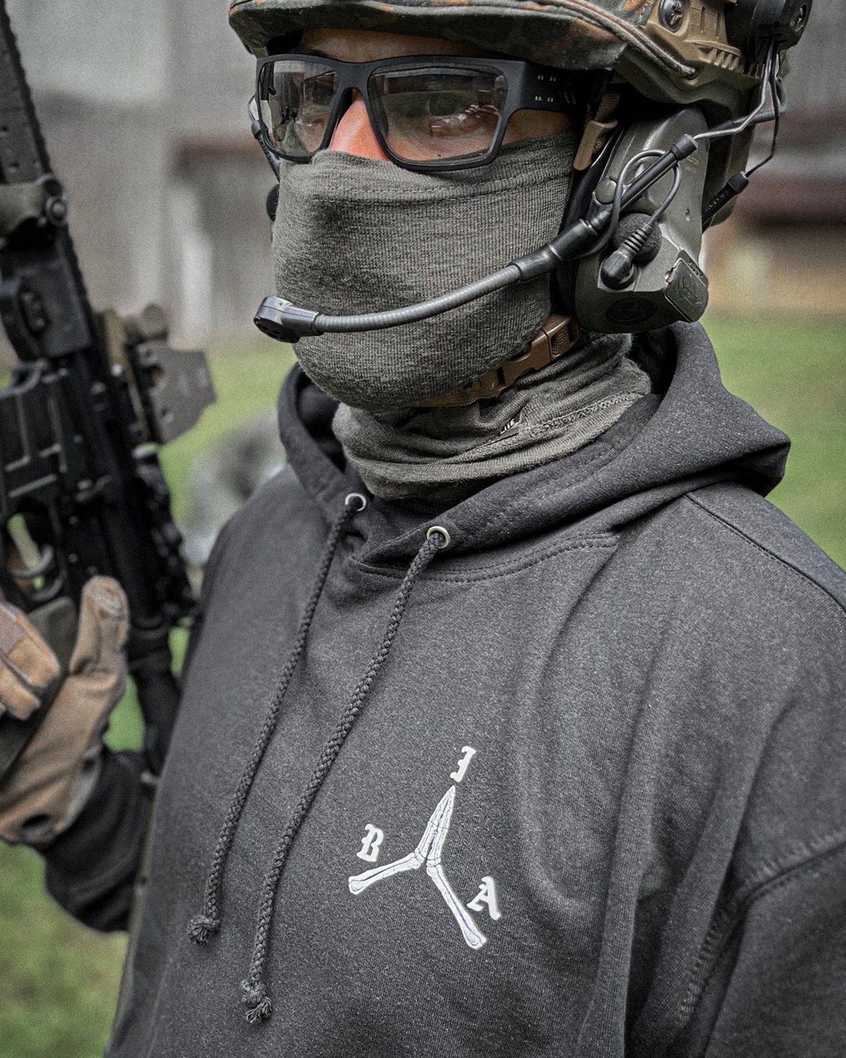 Man in helmet and neck gaiter wearing the black Brothers in Arms Hoodie, rifle at the ready