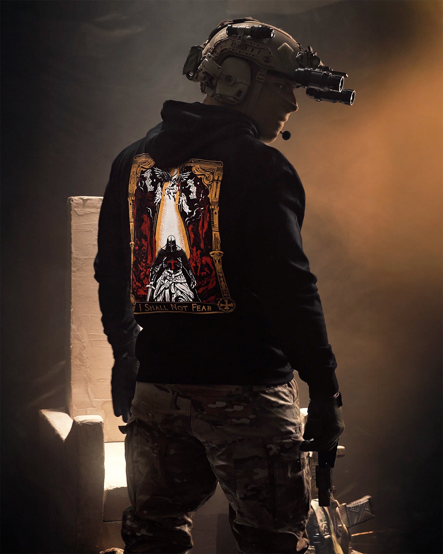 Person in tactical gear with a dark-themed design on the back, standing in a dimly lit environment. #color_black #in_action. #color_black #in_field