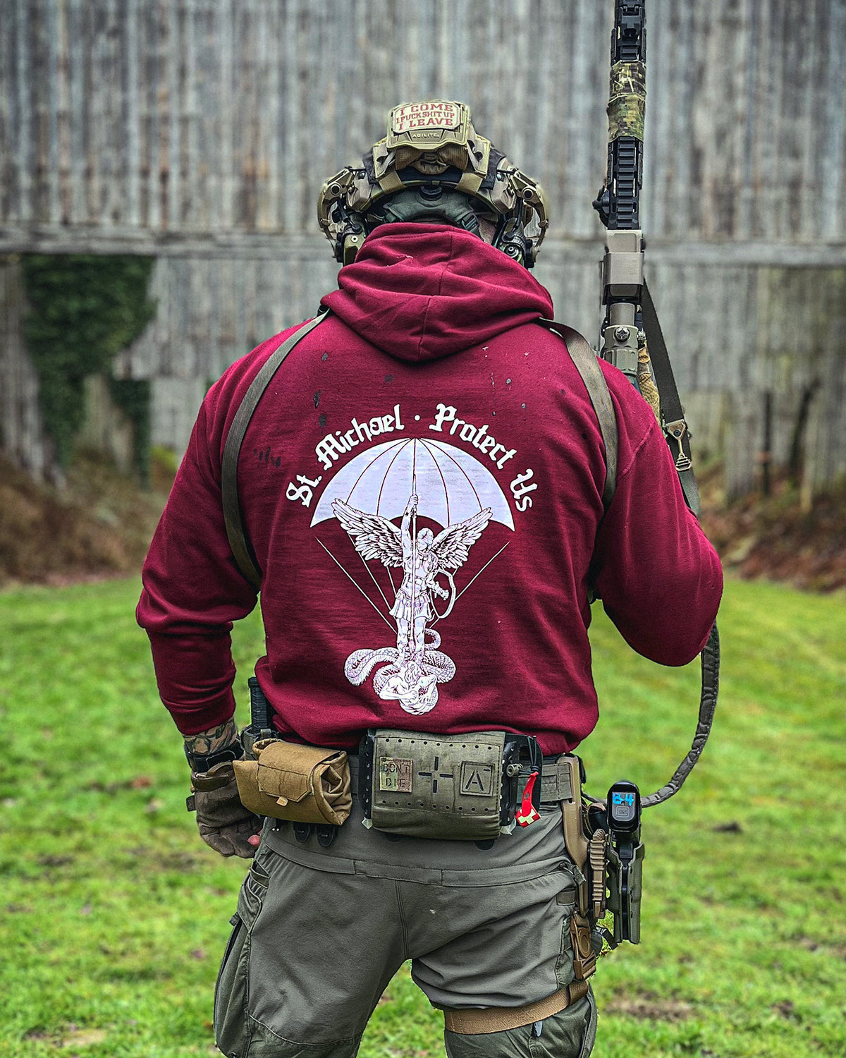 Man from behind in the bordeaux St. Michael Hoodie with a rifle on a training ground