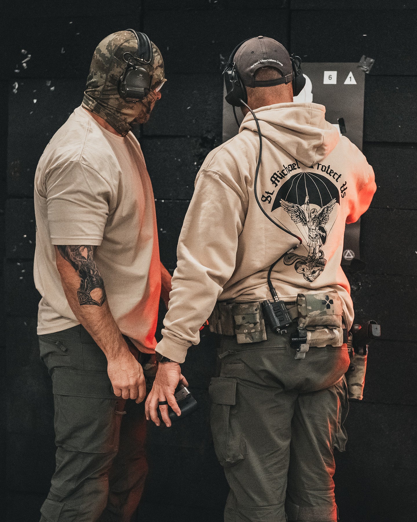 Two men at an indoor range, one from behind in the sand St. Michael Hoodie #color_sand #in_field