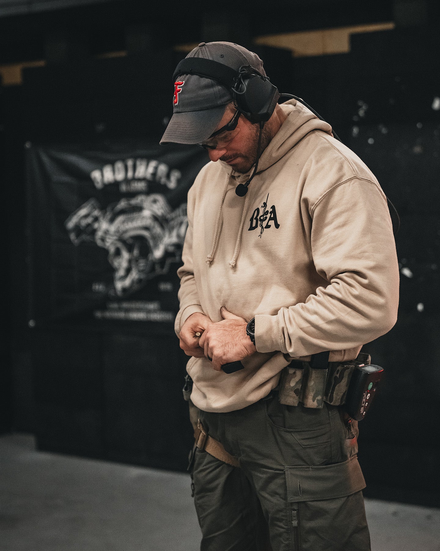 Man in a cap wearing the sand St. Michael Hoodie at an indoor shooting range #color_sand #in_field
