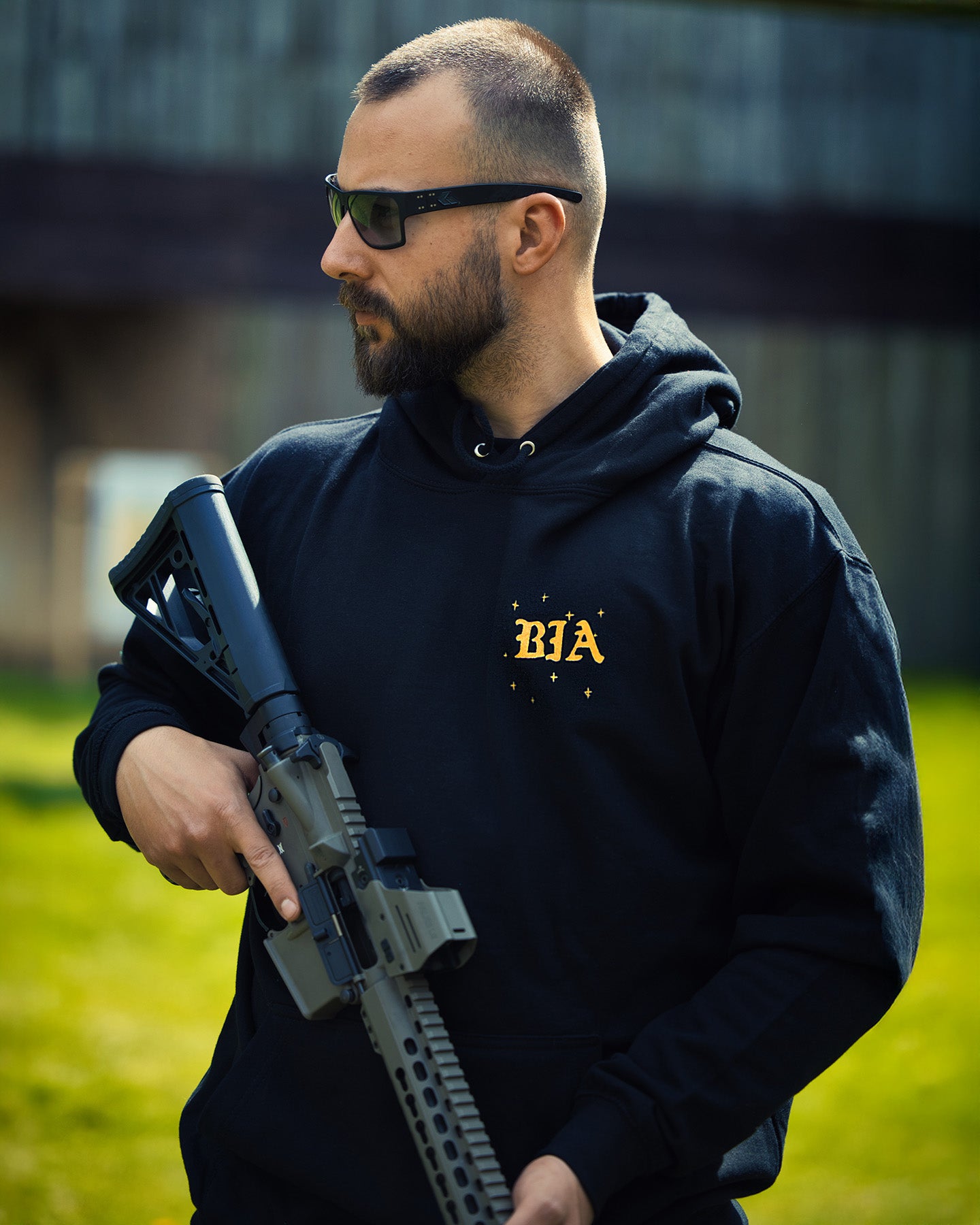 Man with a rifle wearing the black Eyes On The Stars Hoodie, gold chest print #color_black #in_field