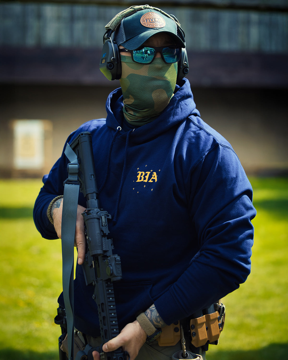 Man with a rifle and ear protection wearing the navy Eyes On The Stars Hoodie