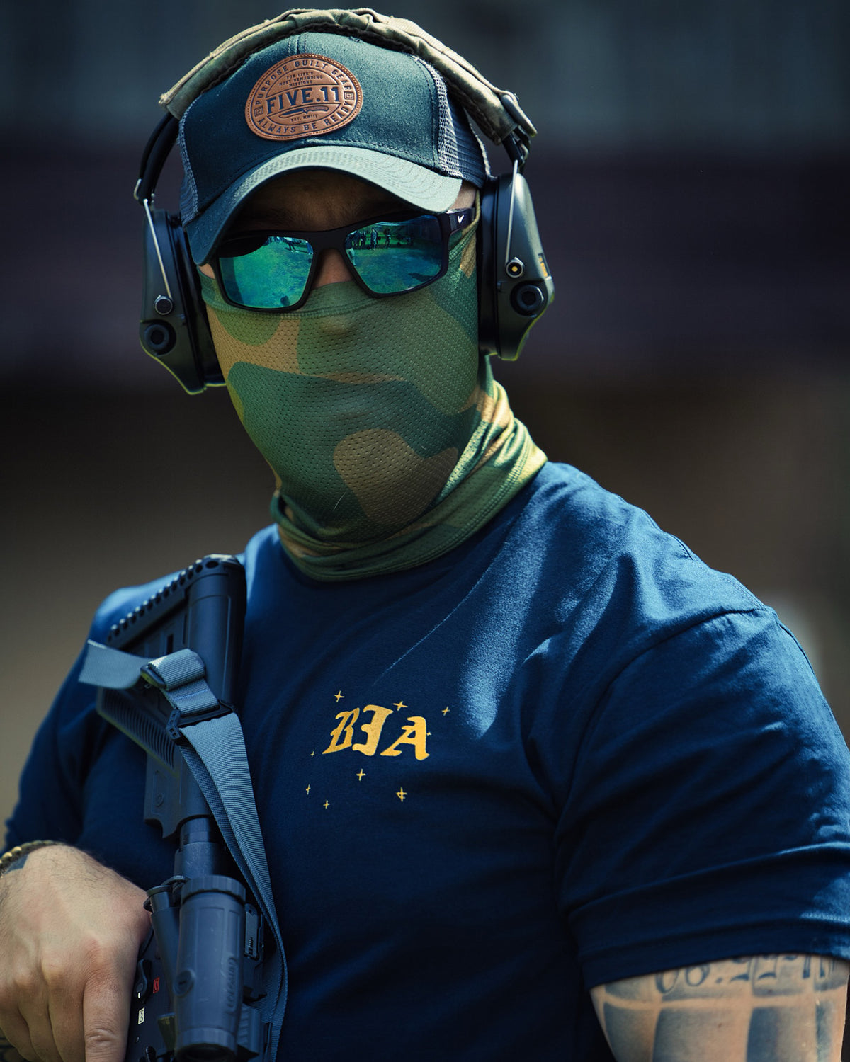 Shooter in a cap and ear protection wearing the navy Eyes On The Stars T-Shirt at the range