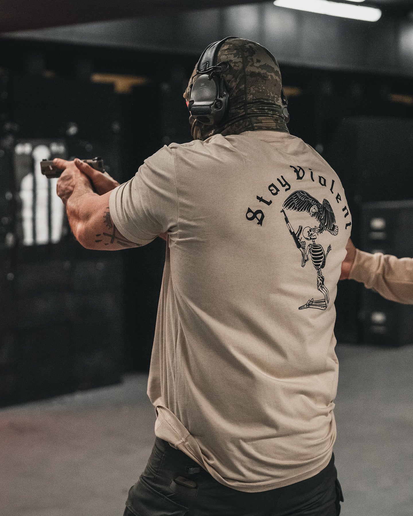 Man from behind in the sand Stay Violent T-Shirt at the range, back print visible while shooting #color_sand #in_field