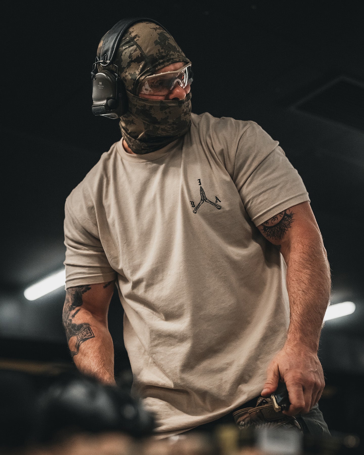 Front of the sand Stay Violent T-Shirt at the range, worn with ear protection and a face covering #color_sand #in_field
